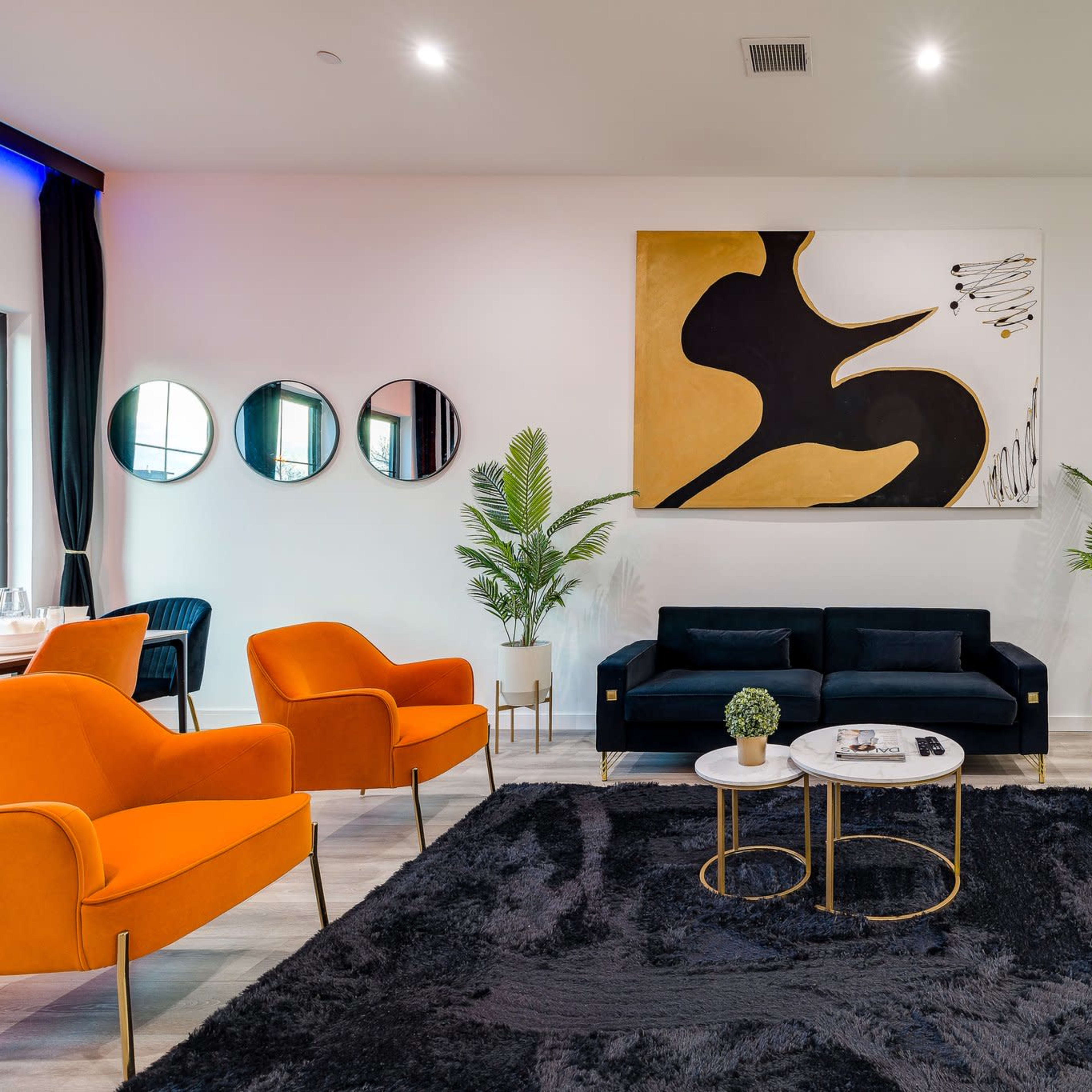 A modern living room with black and orange furniture, a large abstract painting, and round mirrors on the wall.