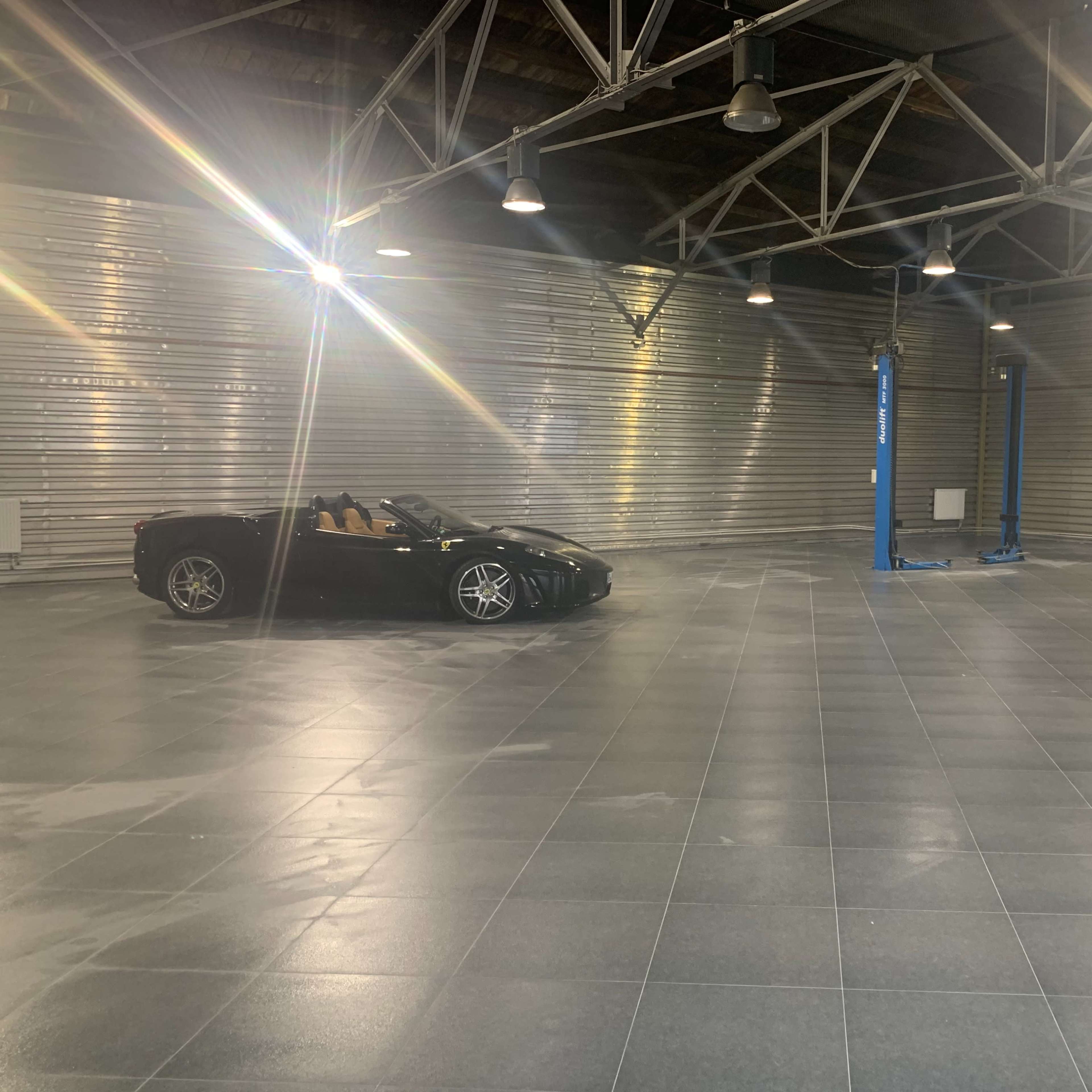 A black convertible sports car is parked in an empty, brightly lit industrial garage with metallic walls.