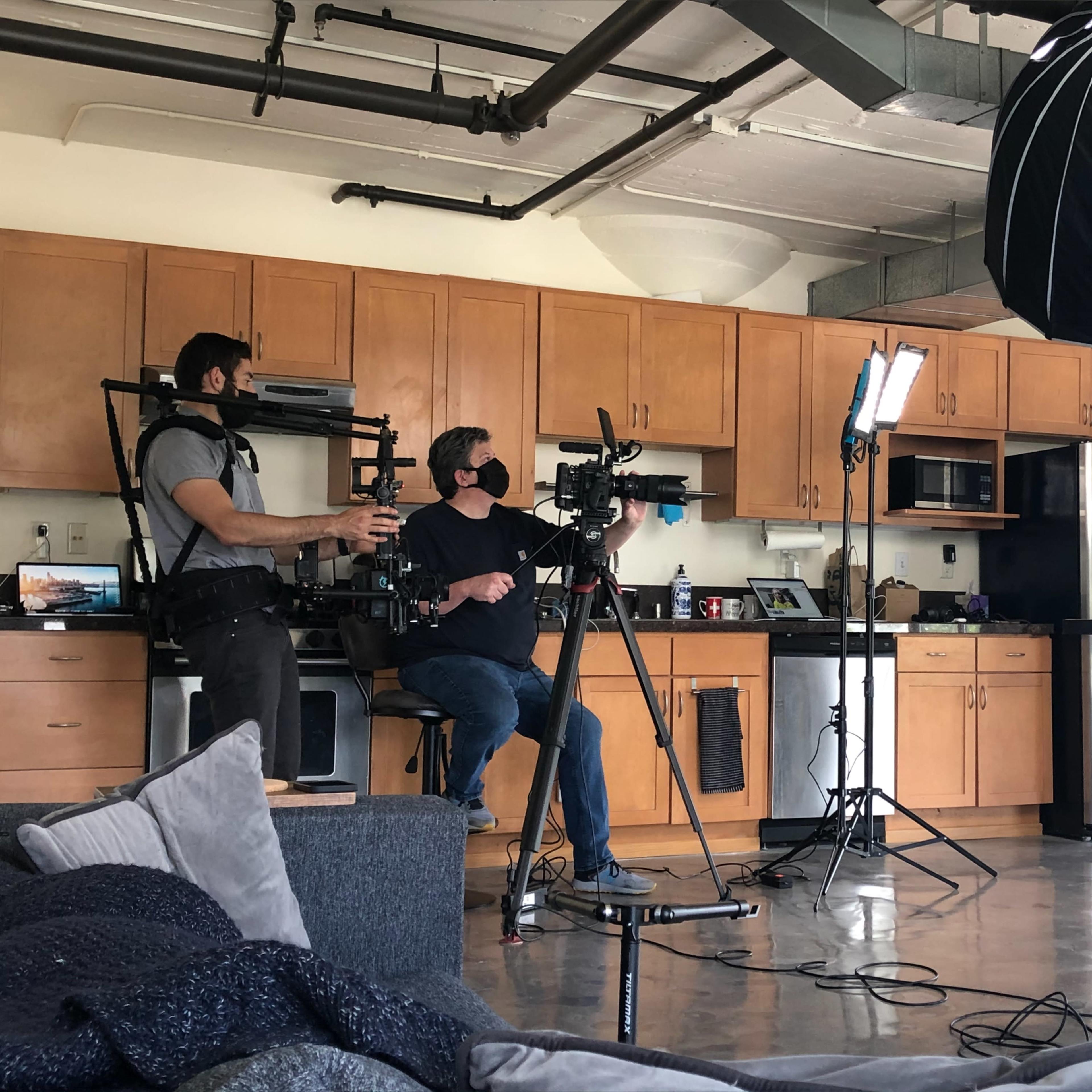 A film crew sets up equipment in a modern kitchen for a video shoot.