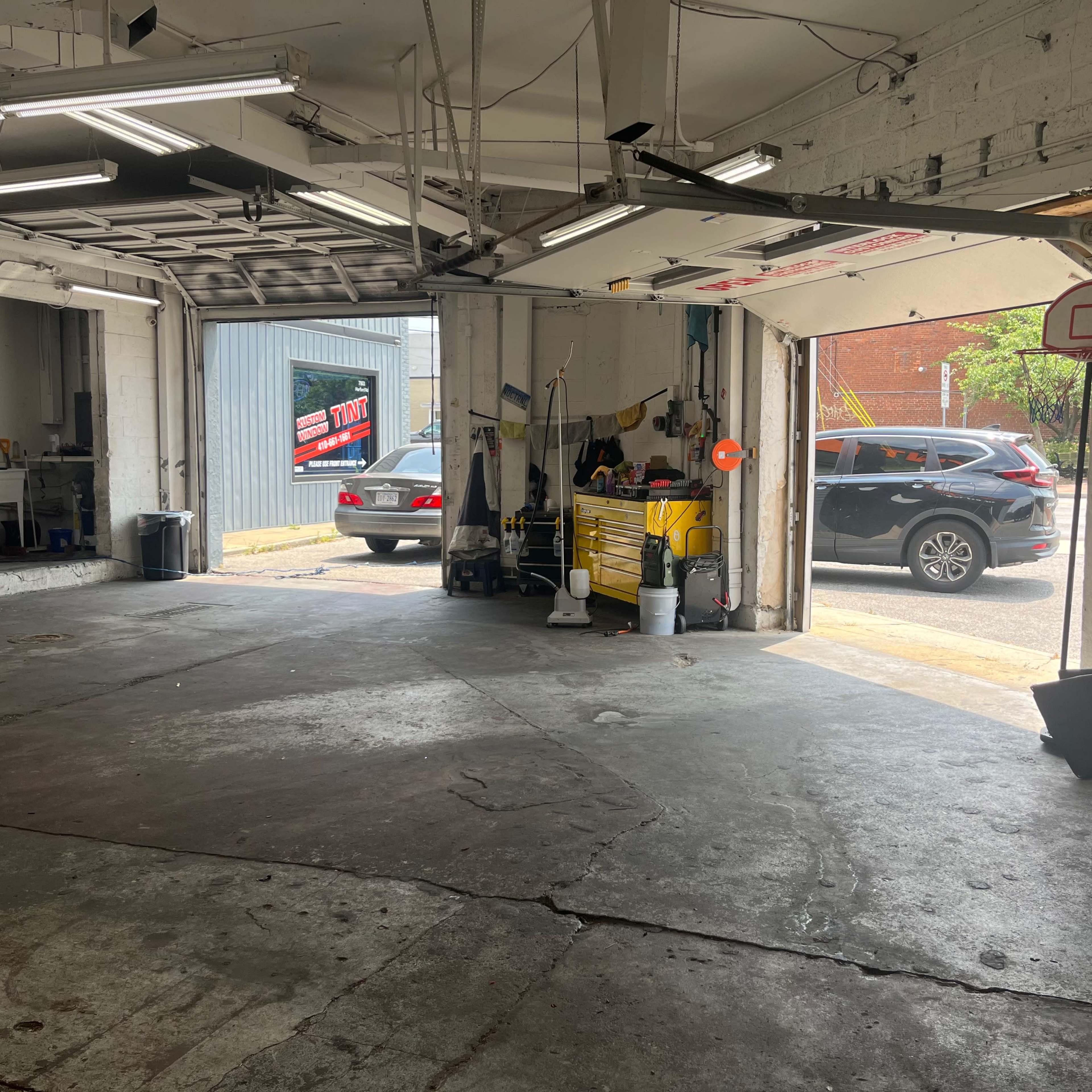 An auto repair garage with tools, a red tool chest, and an open garage door leading to a parking area.