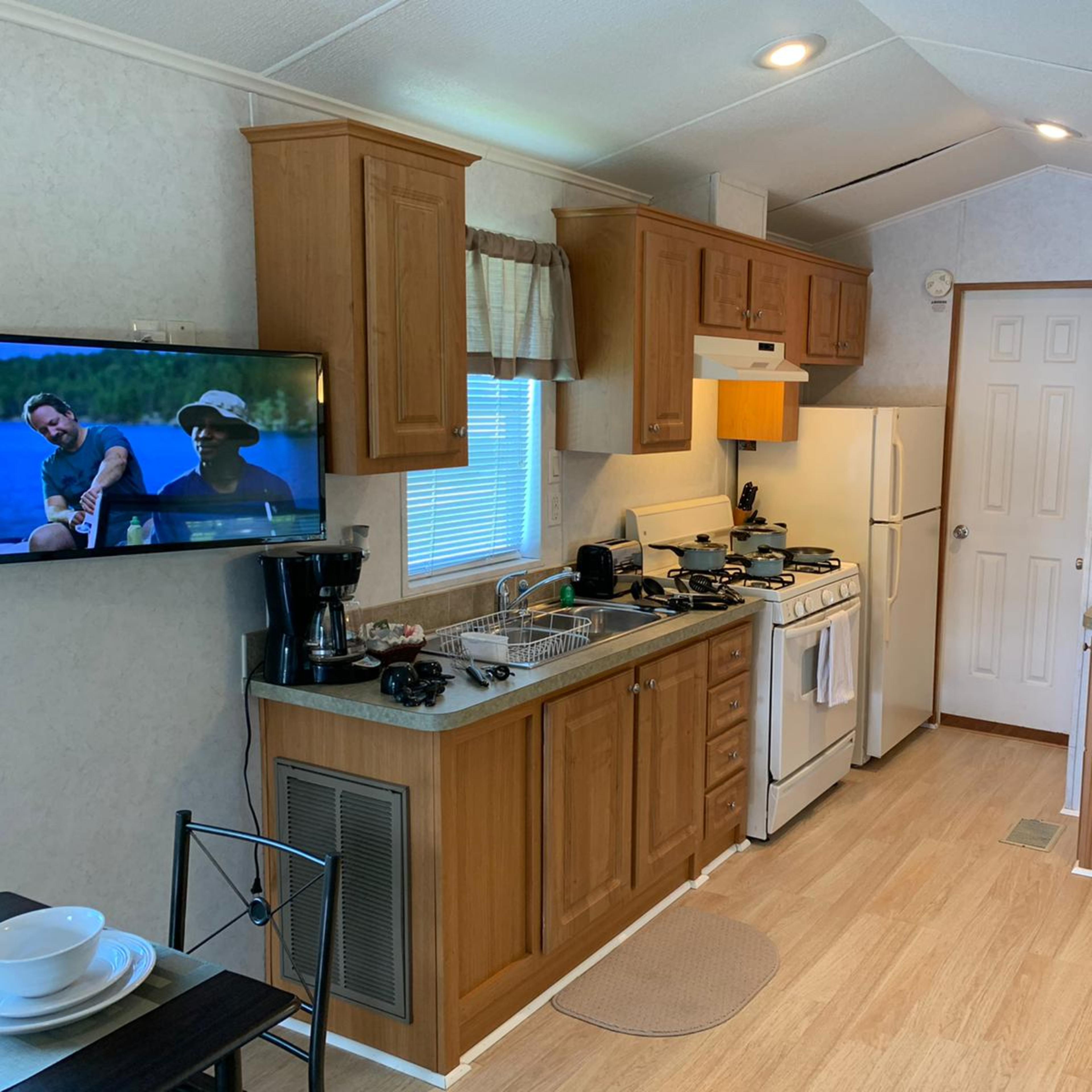 A compact kitchen area in a mobile home, featuring a stove, refrigerator, and a television mounted on the wall.