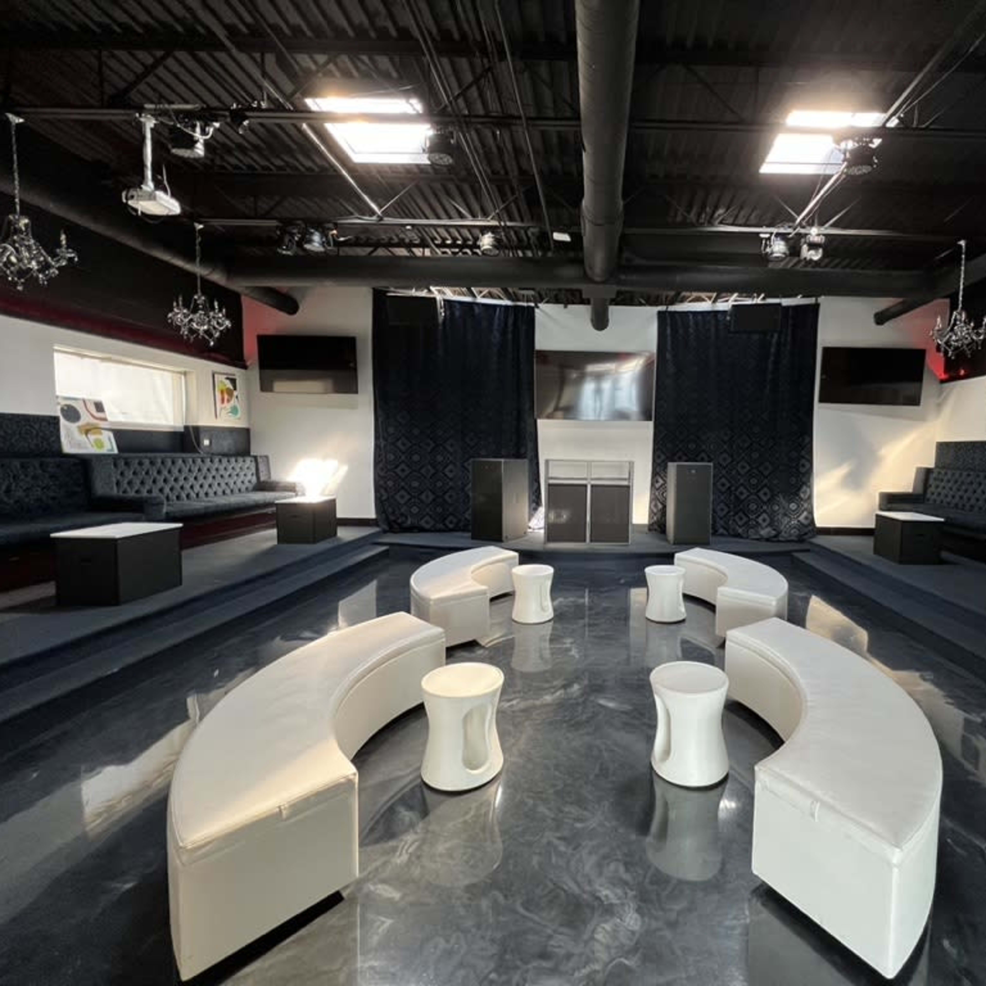 A modern lounge area with circular seating arrangements, white tables, and dark walls adorned with artwork.