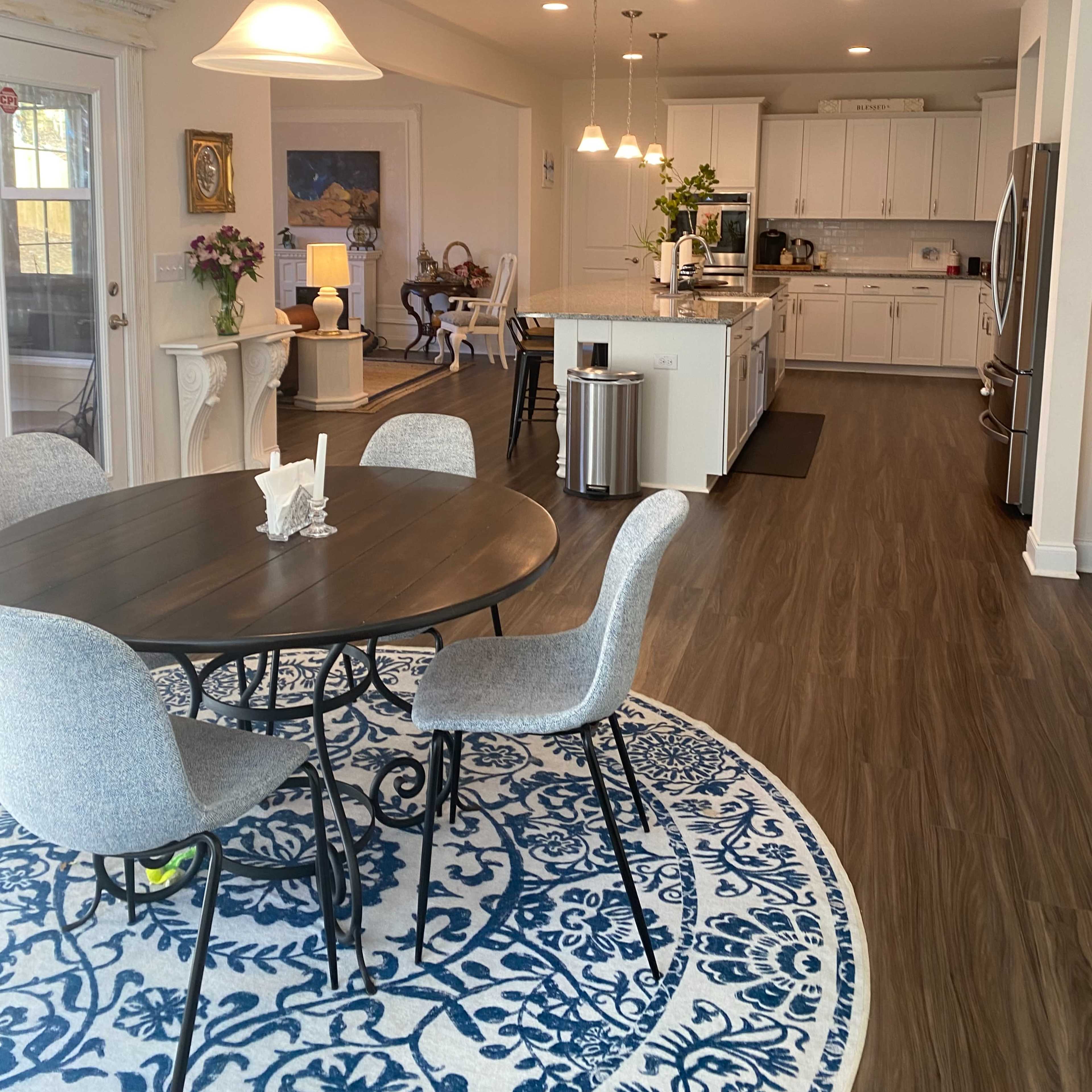A dining area with a round table and four chairs is situated near a kitchen that features modern appliances and white cabinetry.