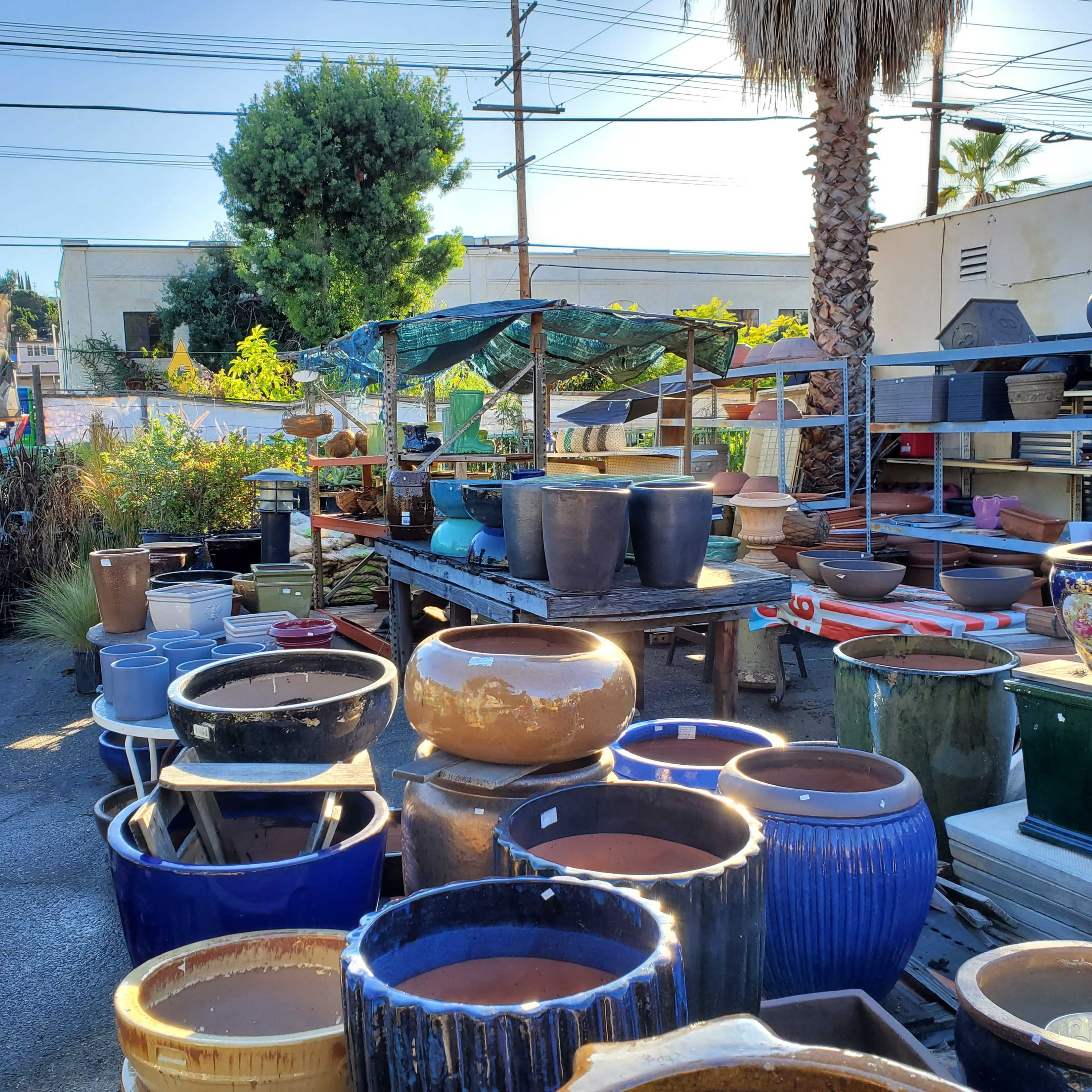 An outdoor garden center filled with various decorative pots and planters displayed on tables and the ground among greenery and trees.