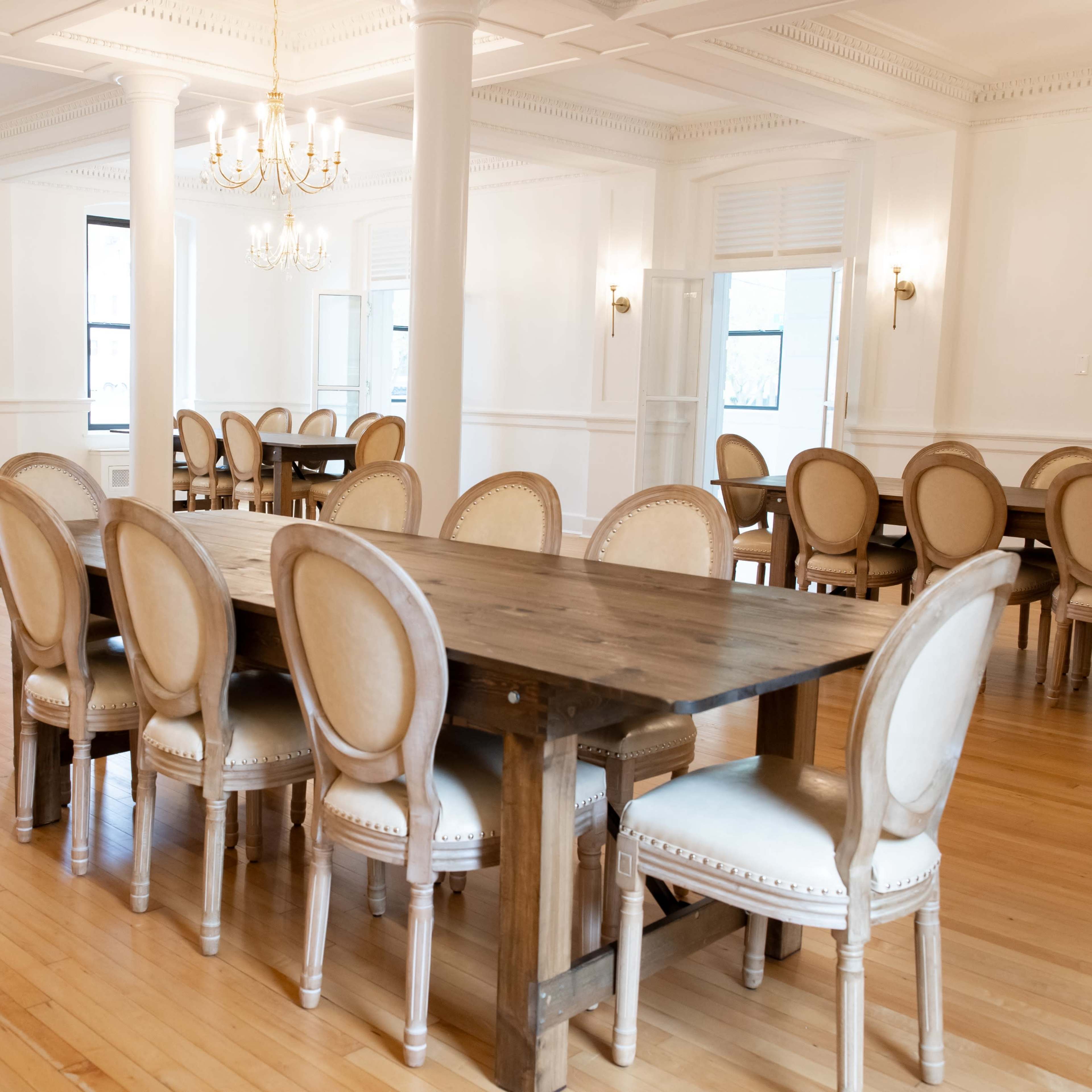 A spacious, well-lit dining area with multiple wooden tables surrounded by chairs, all set on a light wooden floor.