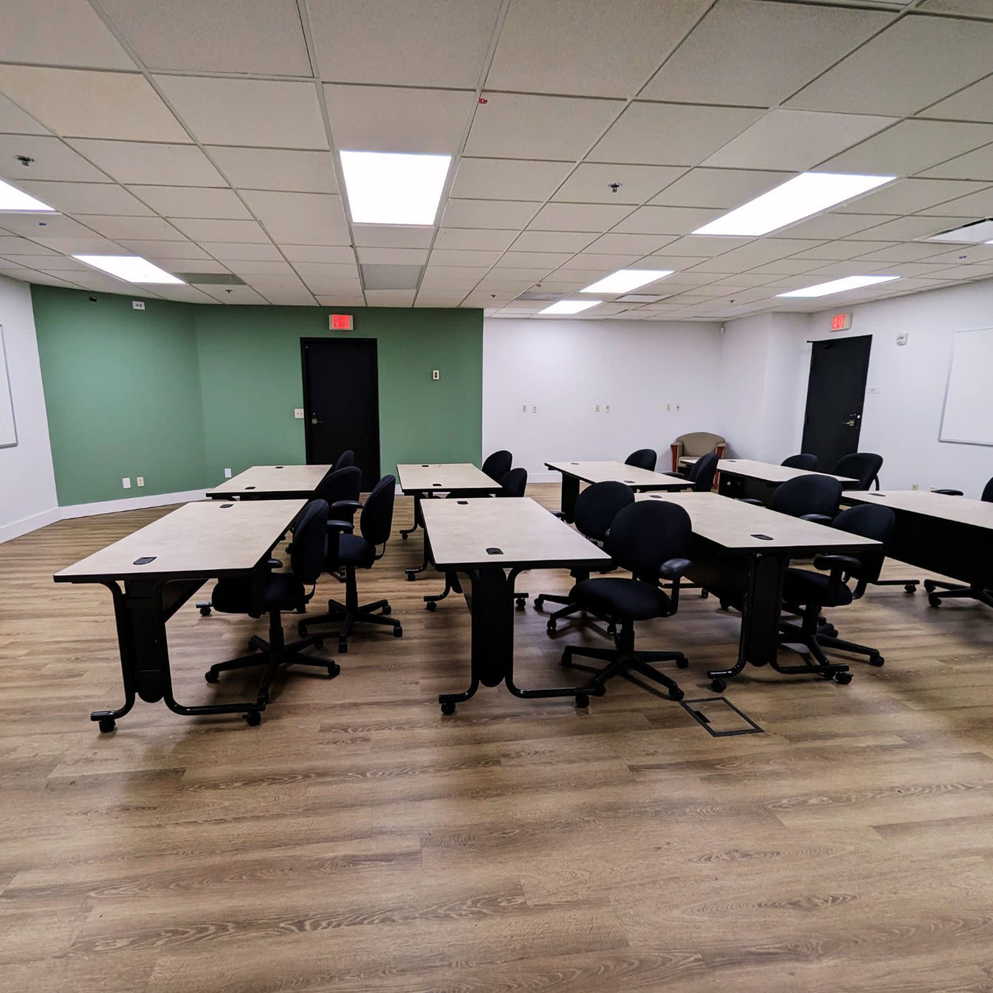 A classroom with multiple desks arranged in a U-shape, surrounded by green and white walls and equipped with a black presentation cart.