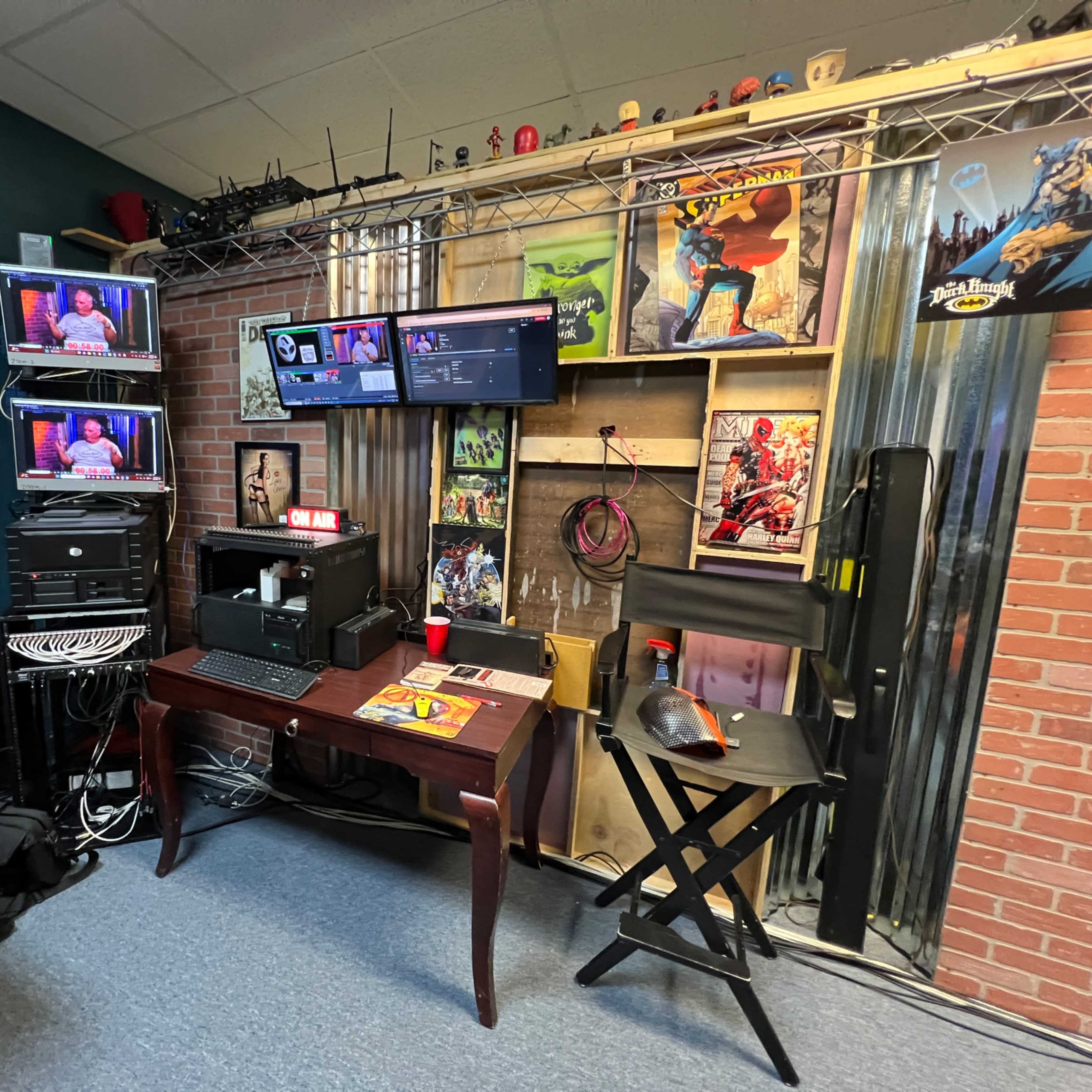 A multimedia production studio equipped with various monitors, a mixing console, and a cluttered backdrop displaying posters and storage.
