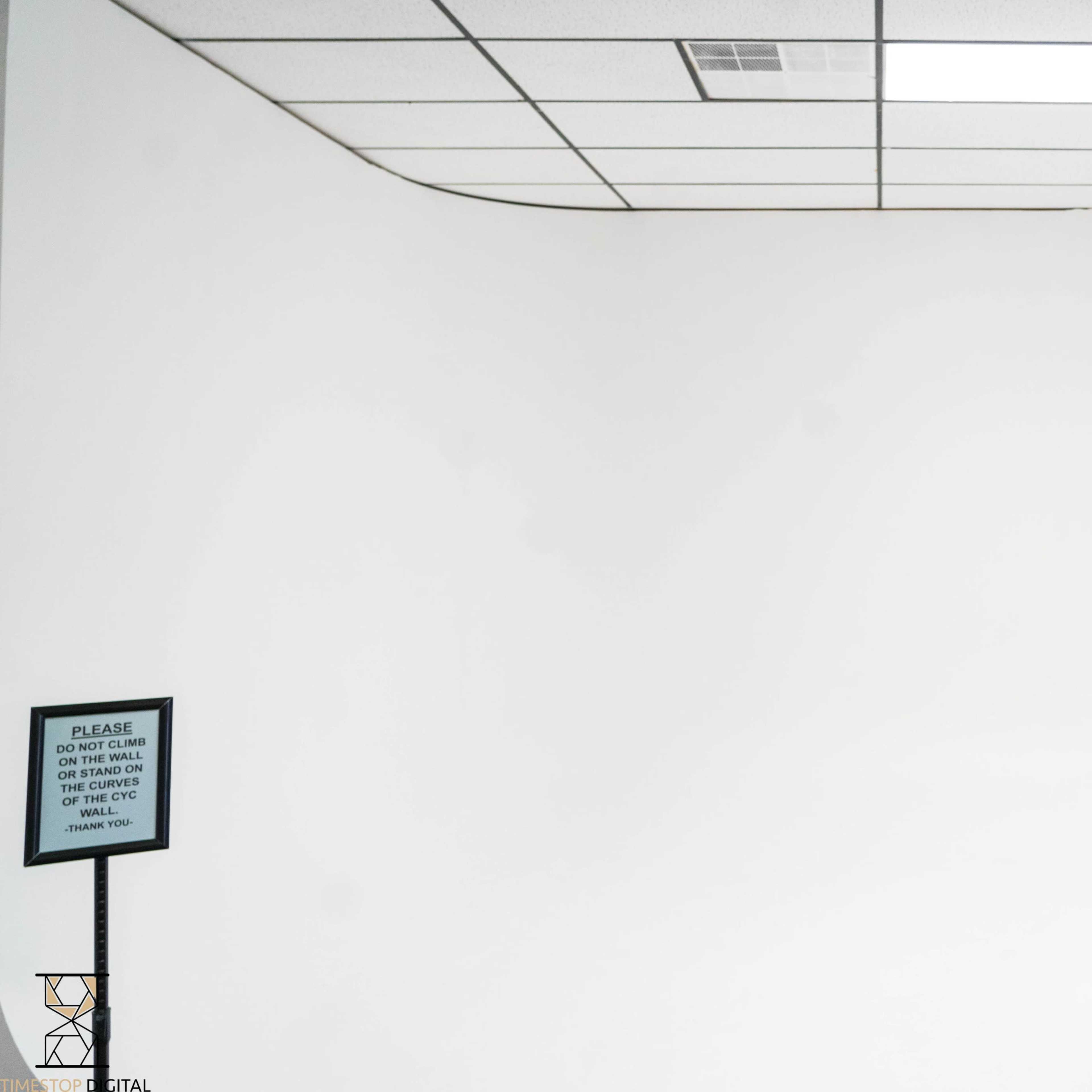 A blank white room with a smooth curved wall and a sign on the left side.