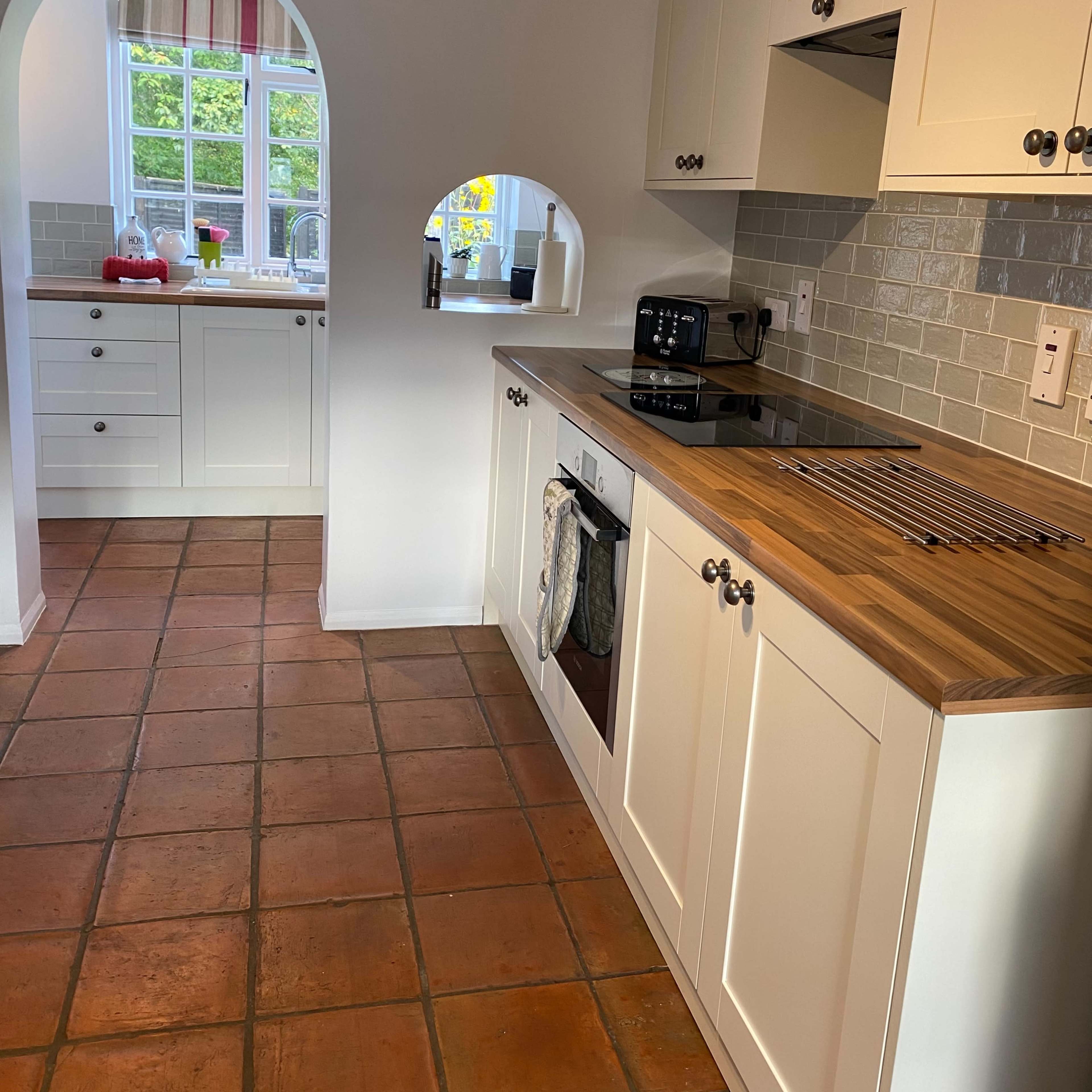 A kitchen with wooden countertops, tiled floors, and white cabinets, featuring an archway leading to another room.