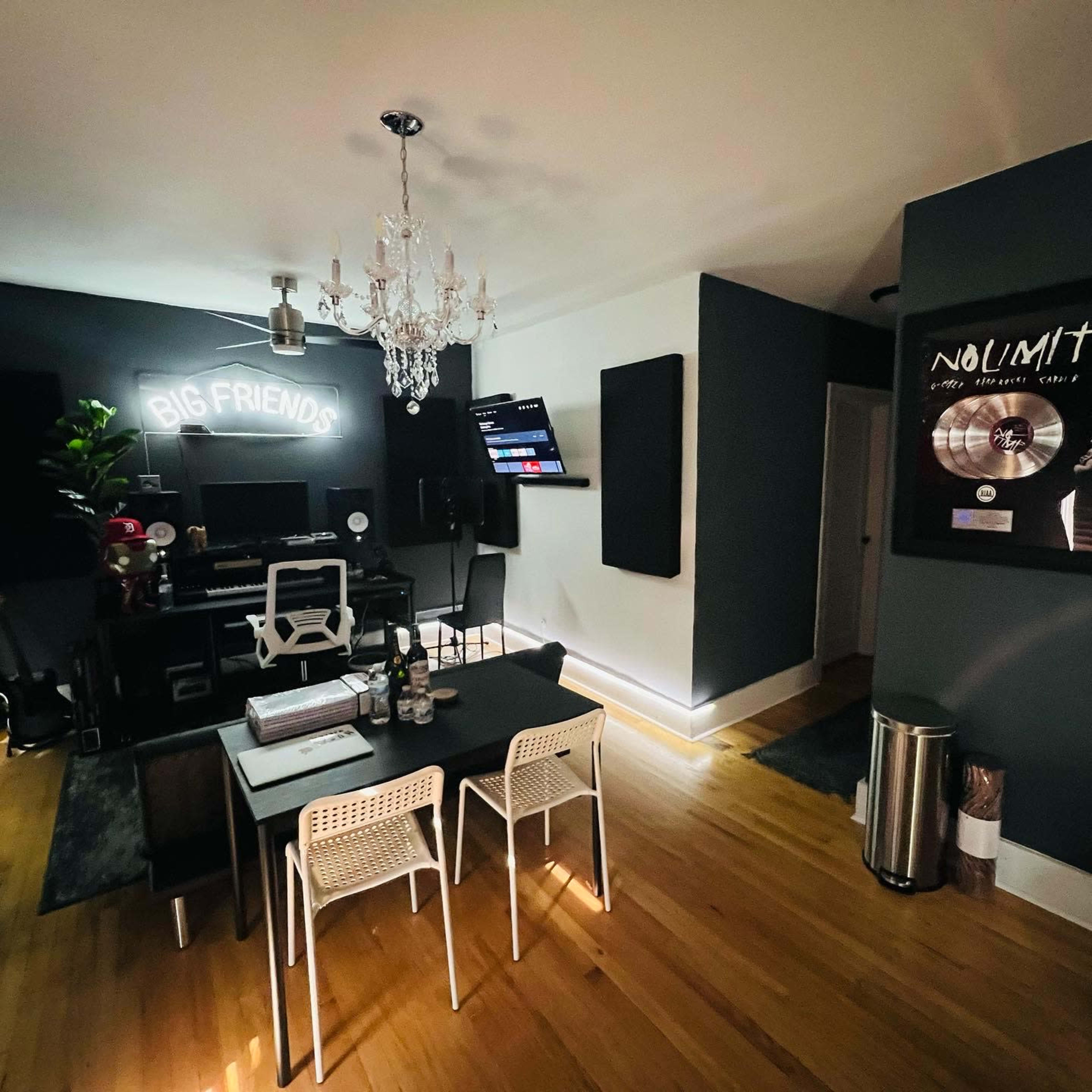 A modern room with a dining table and chairs, a music workstation with a computer, sound-absorbing panels on the walls, and decorative elements like a chandelier and artwork.