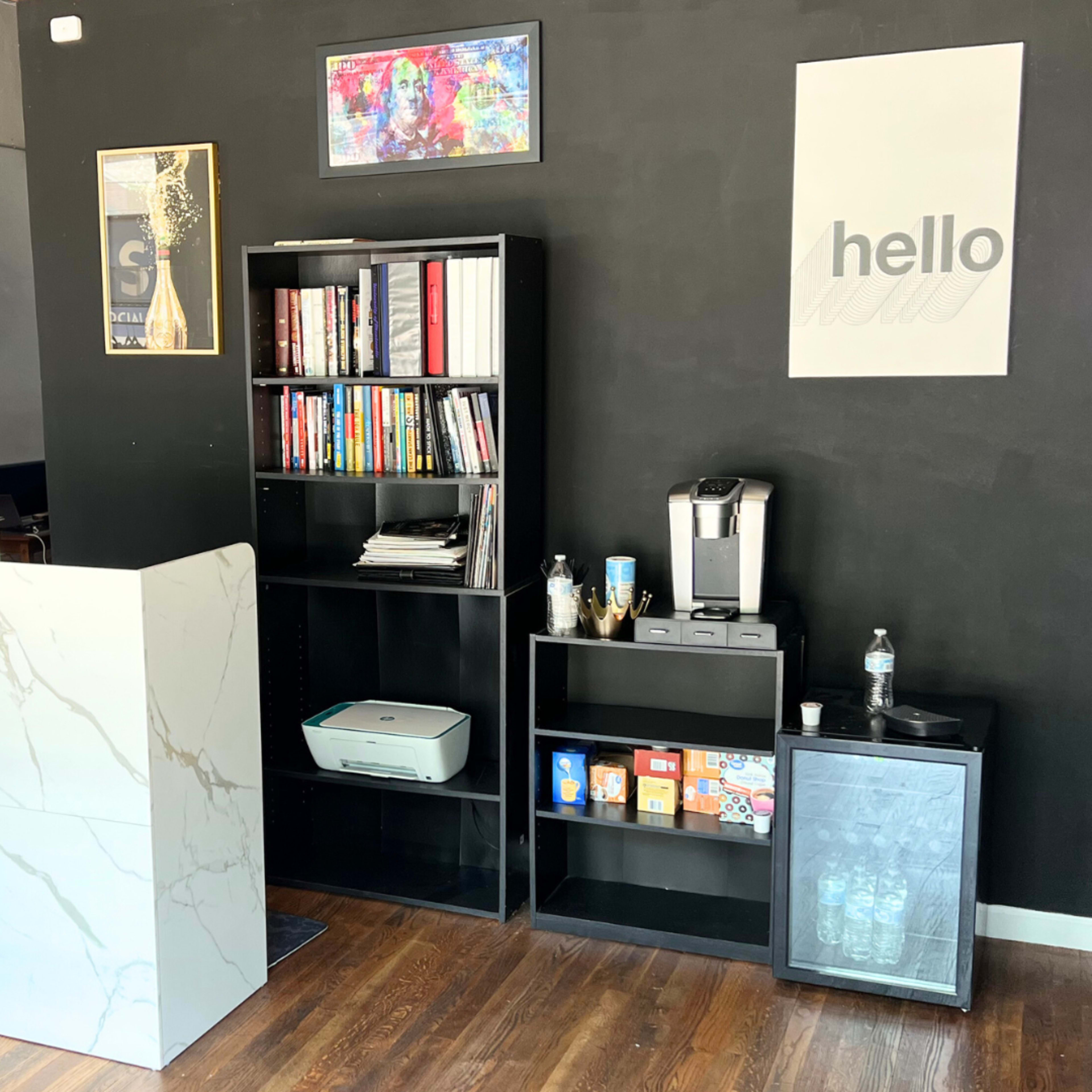 A modern reception area featuring a marble-fronted desk, bookshelves filled with books, a coffee machine, and a television on the wall.