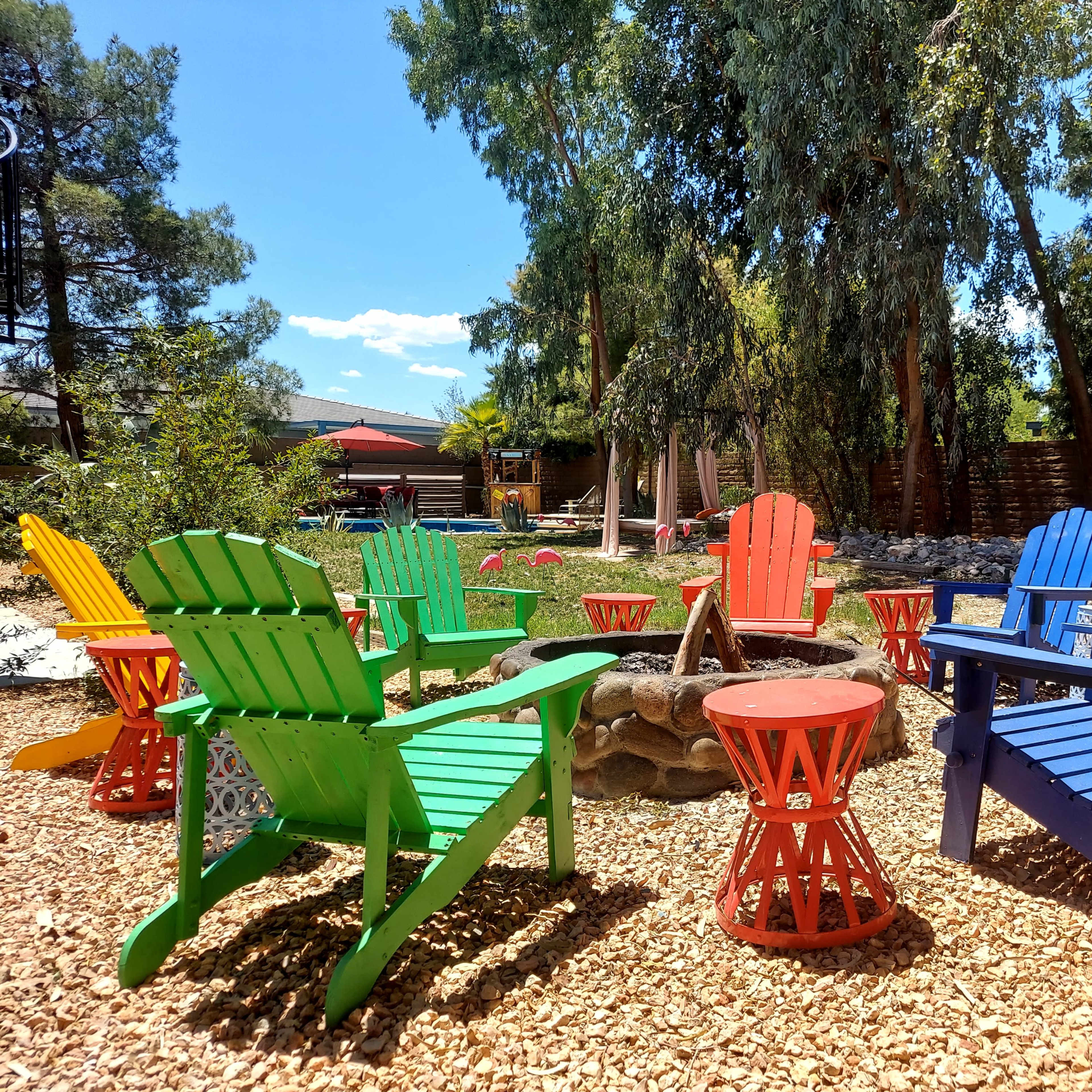A circular seating area with brightly colored Adirondack chairs surrounds a stone fire pit in a landscaped yard.
