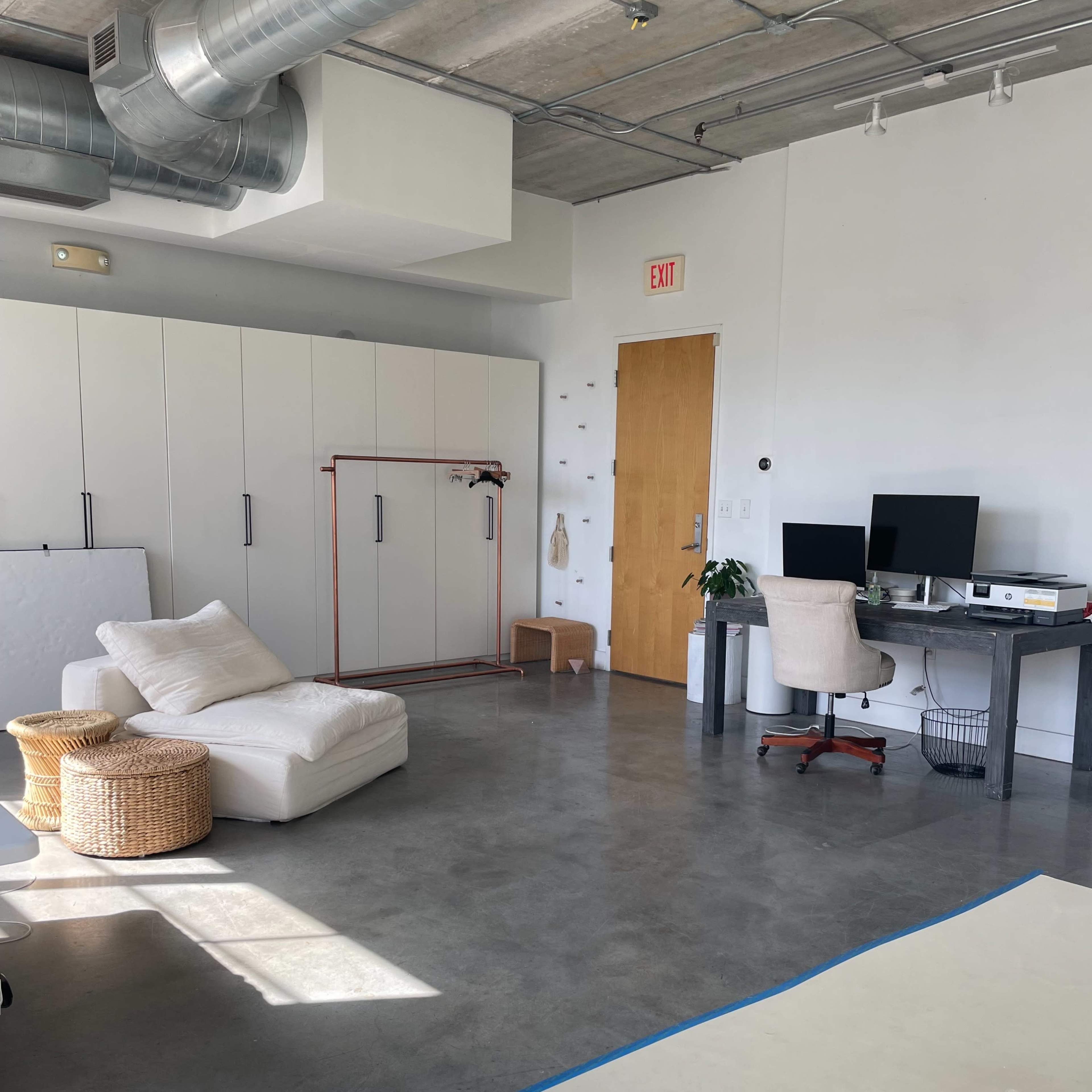 A spacious, minimalist room features a white couch, a desk with a computer, and storage cabinets against the wall.