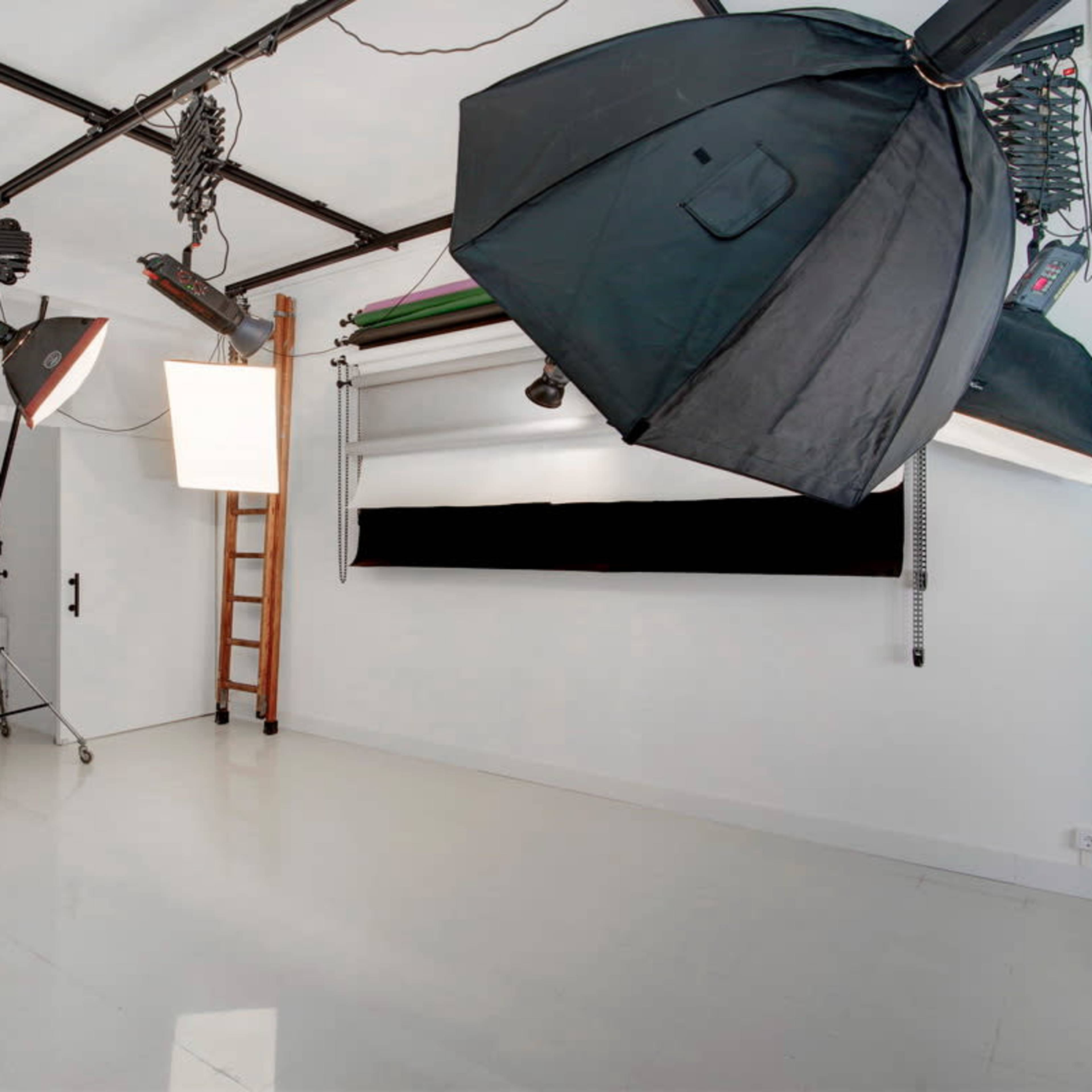 A photography studio with large lights mounted on stands and a seamless backdrop setup against a white wall.