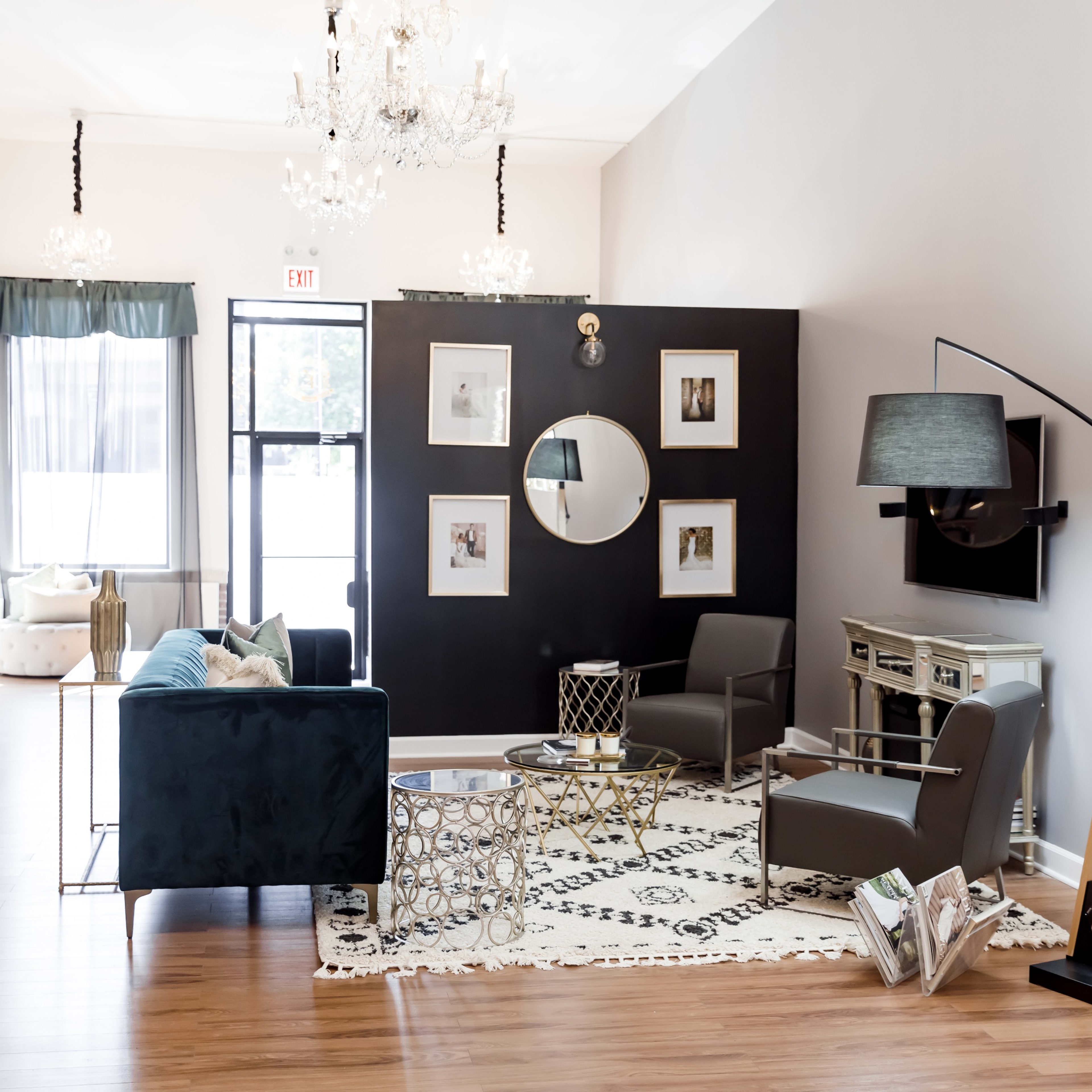 A modern living space with a teal sofa, two gray chairs, a round mirror on a black accent wall, and decorative elements including a coffee table and a floor lamp.
