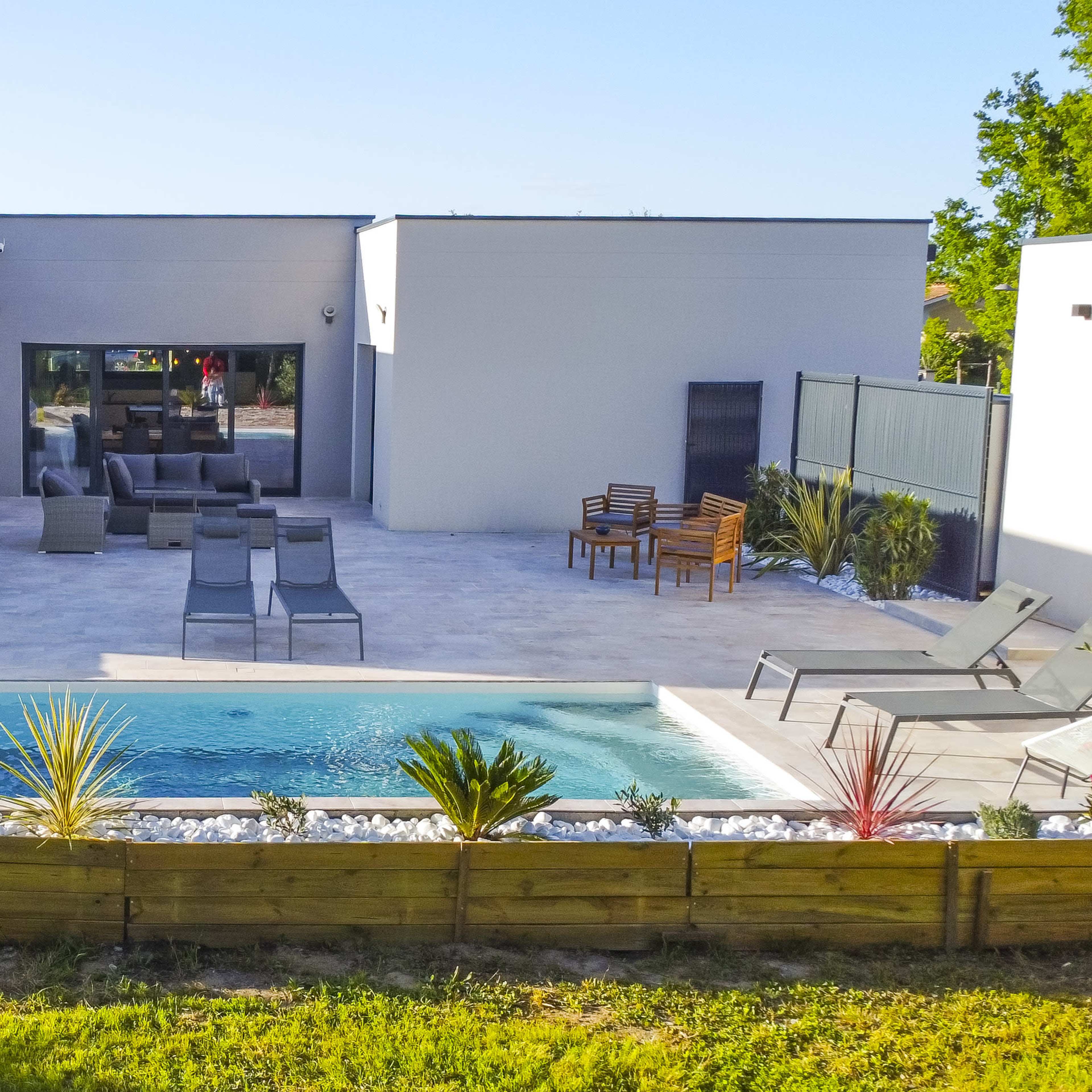 A modern backyard with a swimming pool, hot tub, and seating areas surrounded by landscaped greenery.