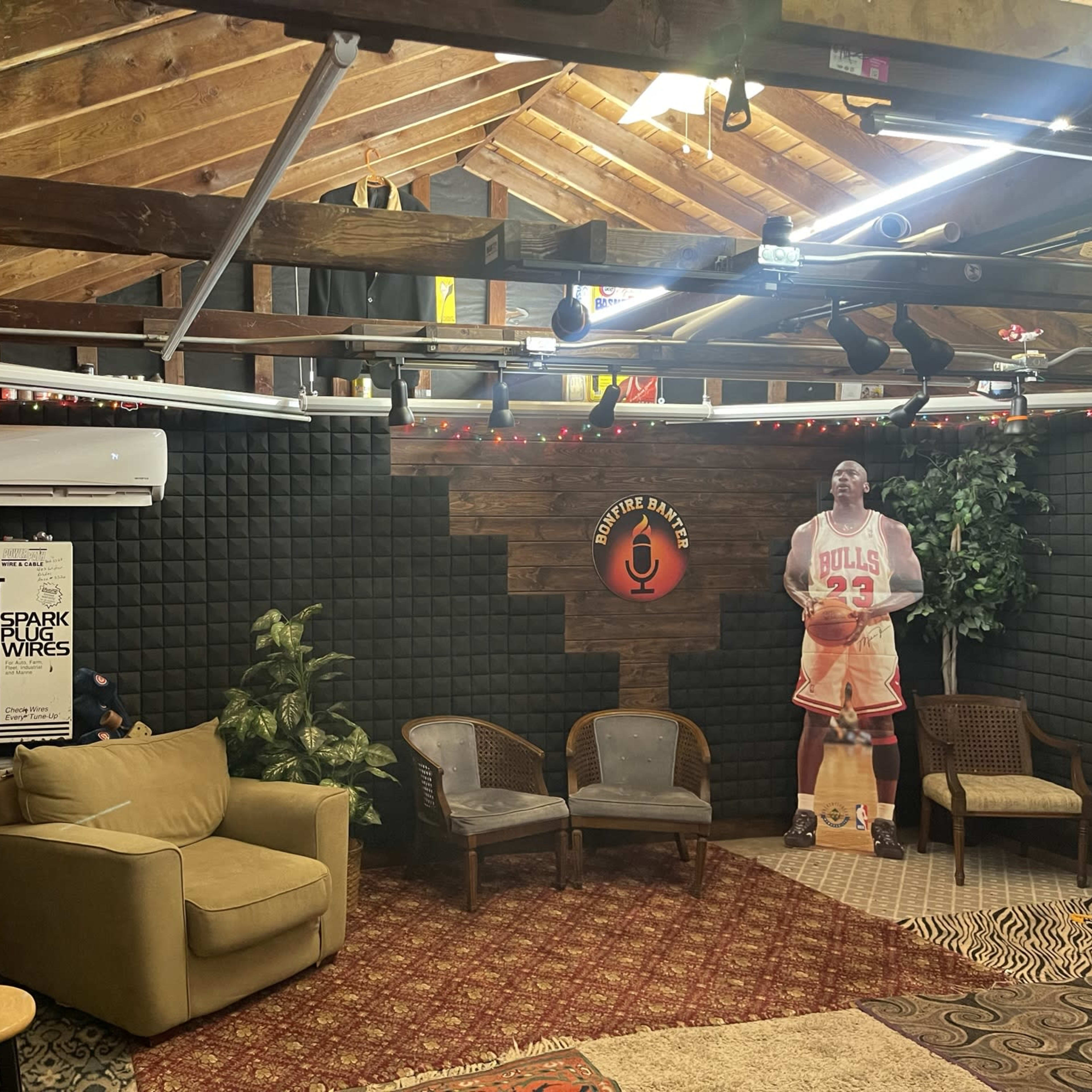 A cozy indoor space with wooden beams and walls, featuring a seating area with a sofa and chairs, decorated with string lights and music instruments.