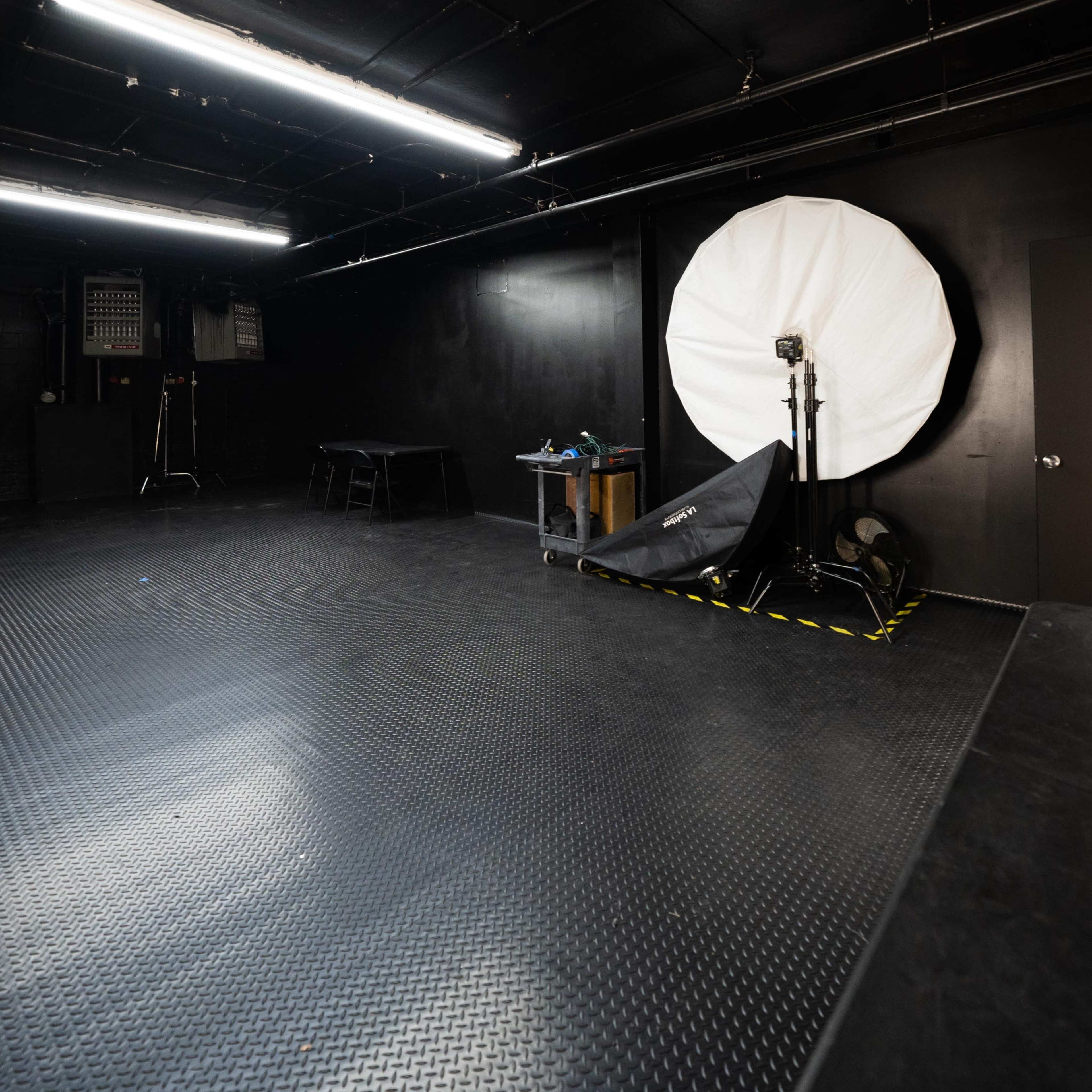 A photography studio with a large white umbrella softbox, a door marked with the number 4, and equipment on a table in the corner.