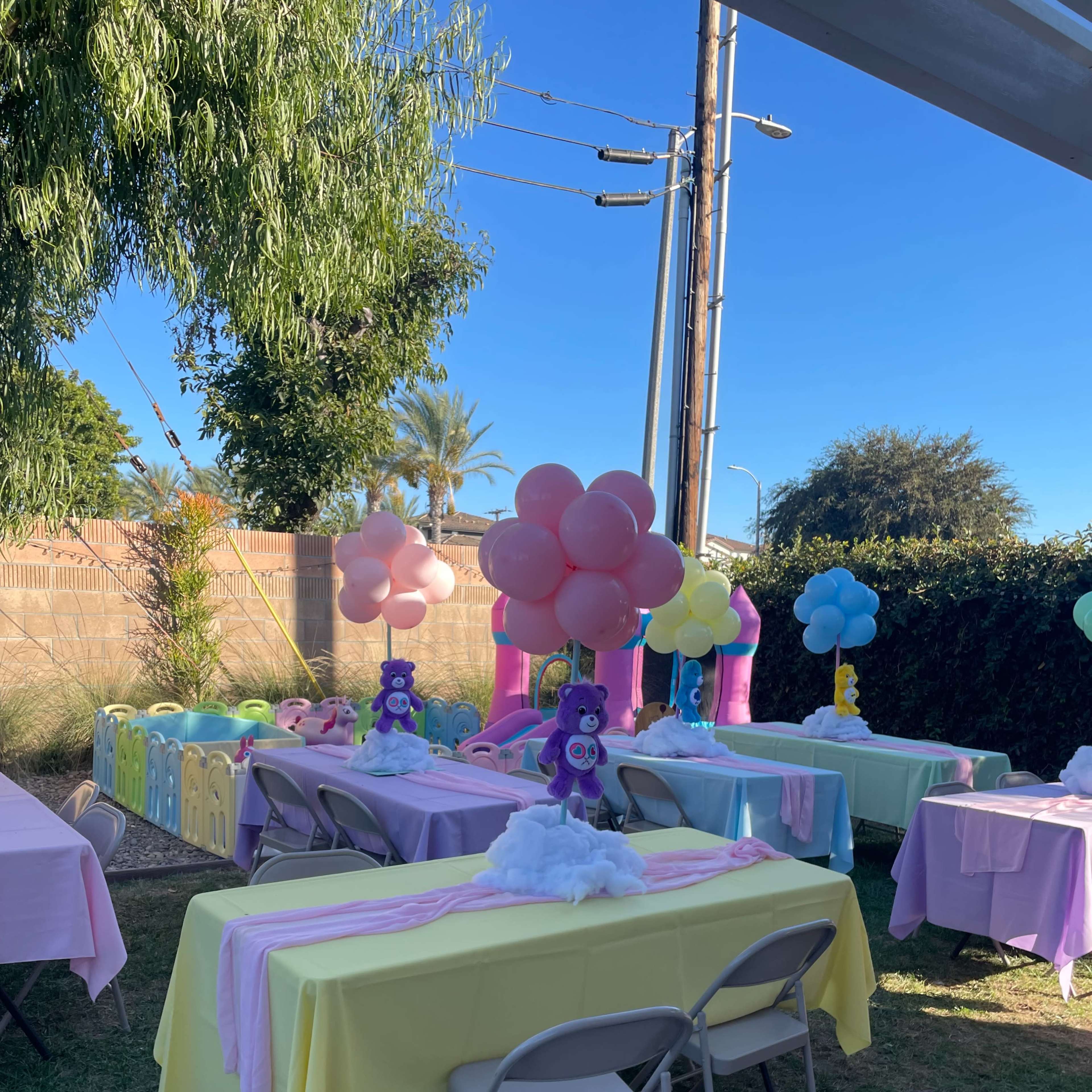 A colorful outdoor party setup with tables covered in pastel linens and decorative balloons in various colors.