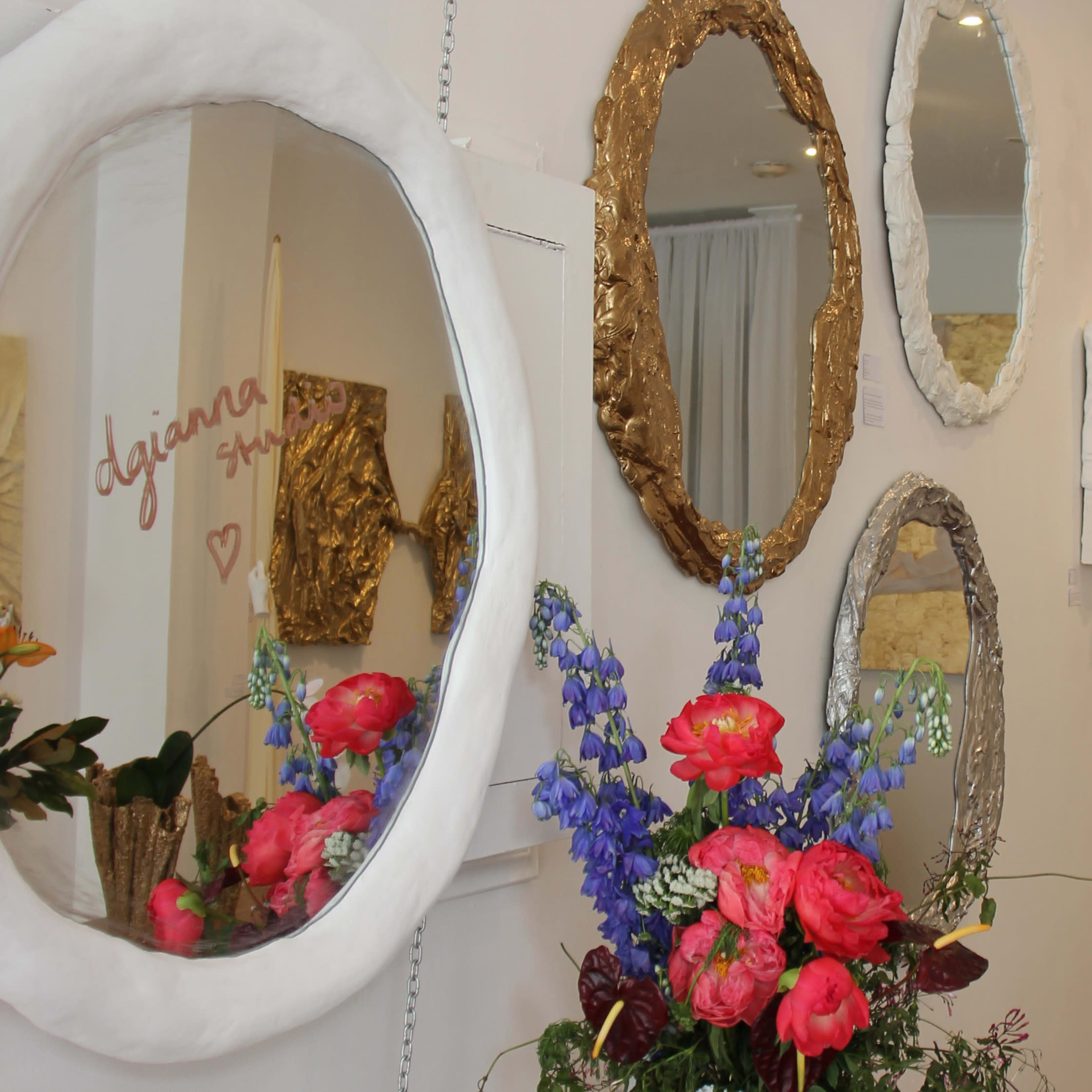 A hallway adorned with decorative mirrors and artworks, alongside a bouquet of colorful flowers placed in front of the mirrors.