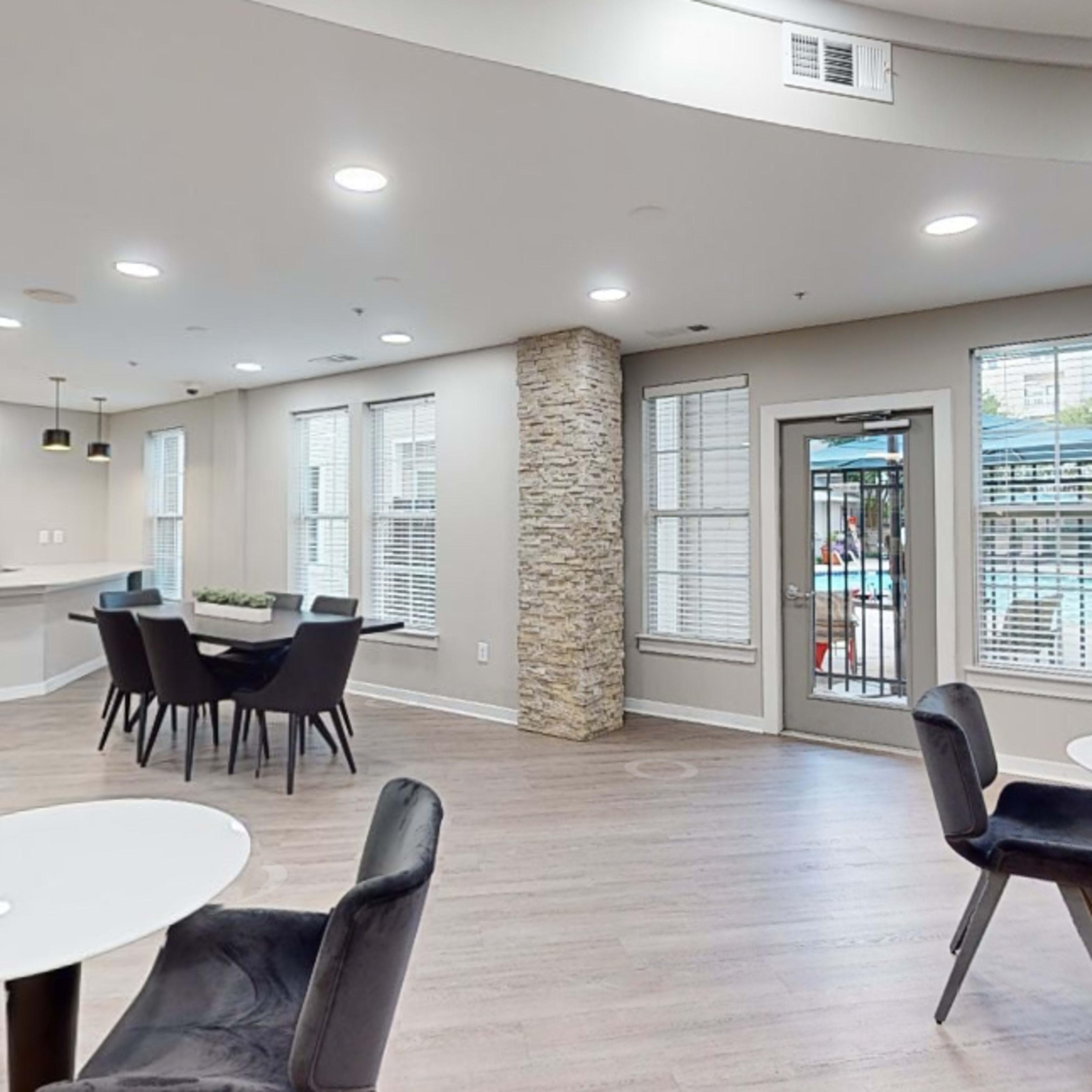 A modern common area with a kitchenette and seating arrangement, featuring a view of a pool area through large windows.
