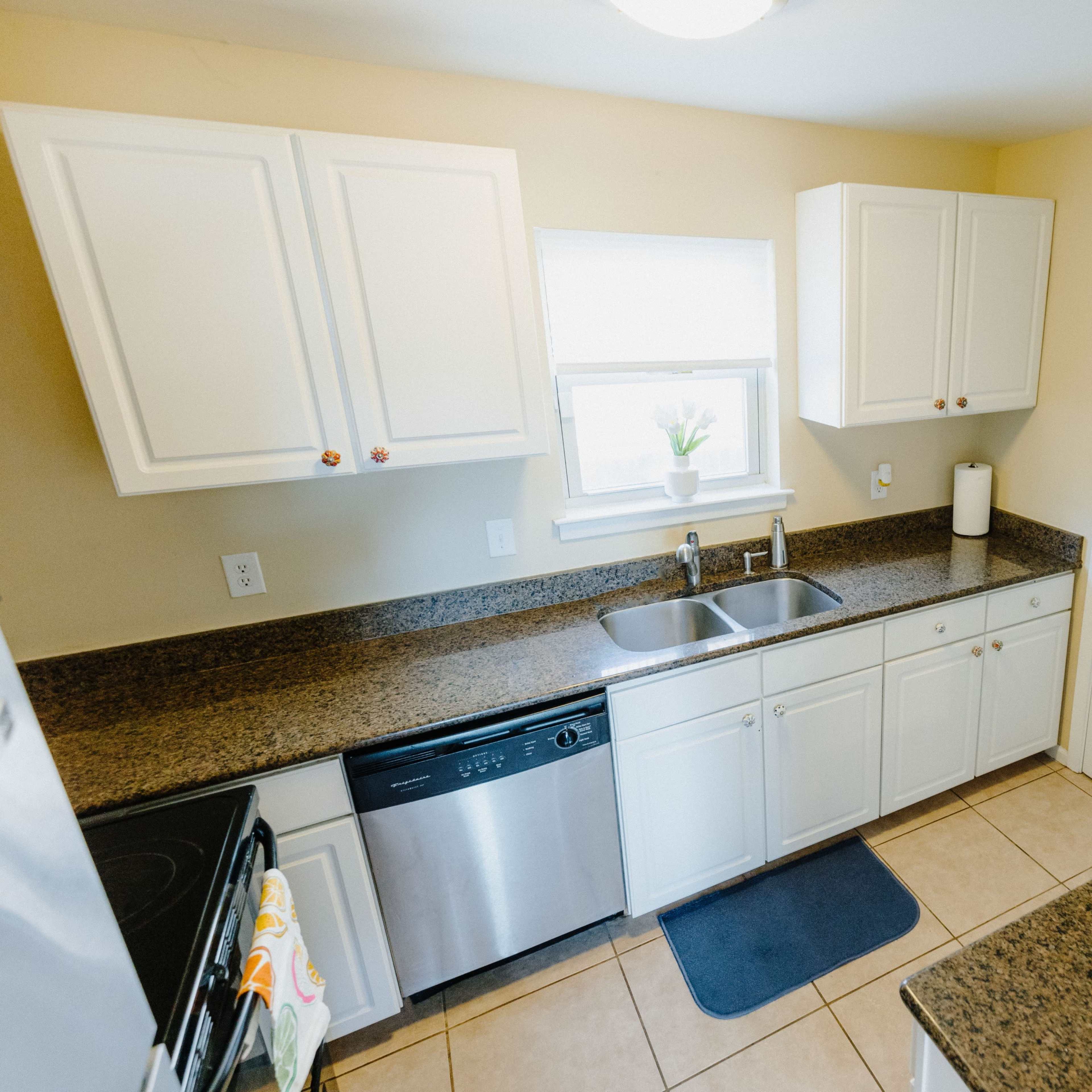 The kitchen features white cabinets, a stainless steel dishwasher, and a countertop with a sink under a window.