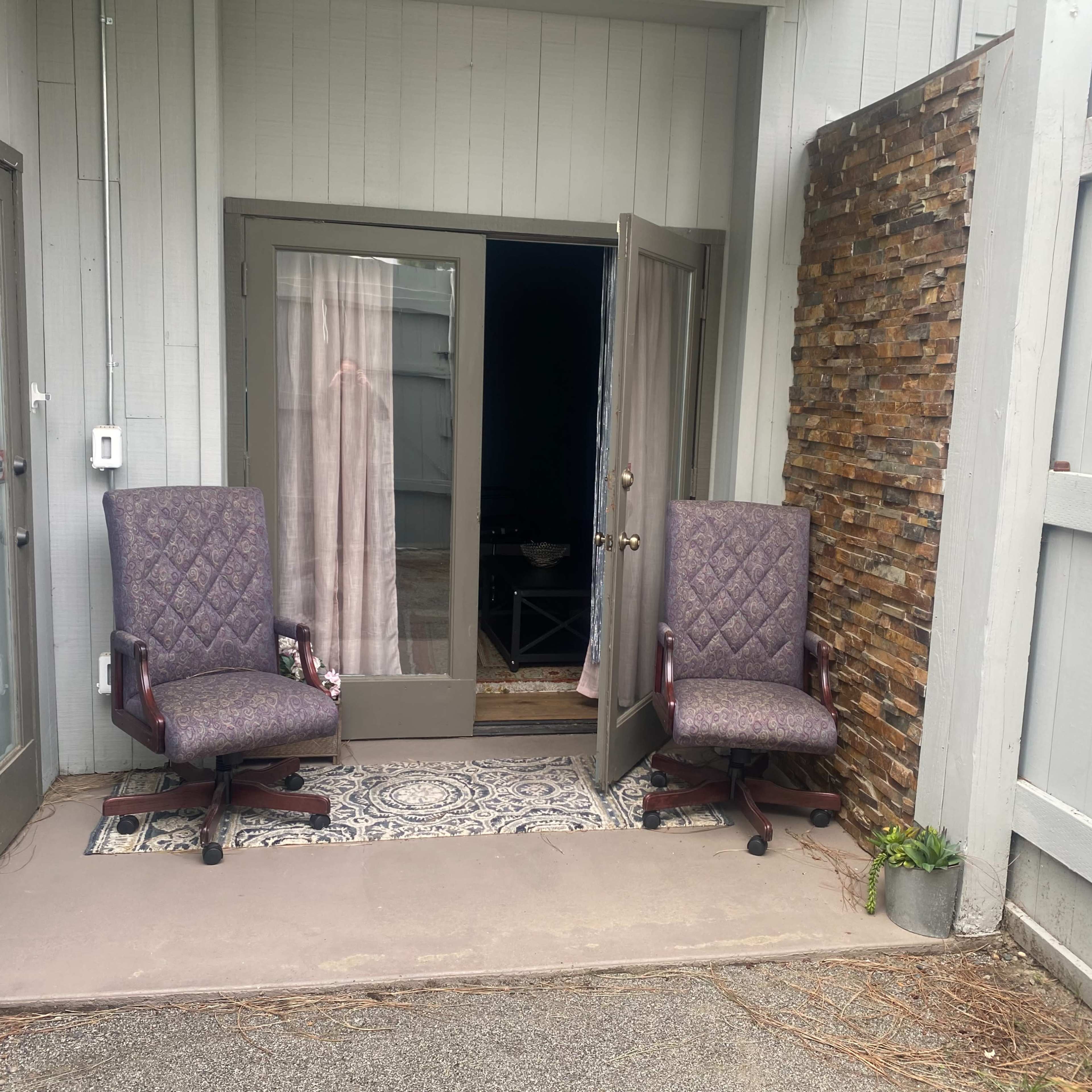 Two upholstered chairs are positioned outside an entrance, flanking a doorway with a patterned rug visible behind it.