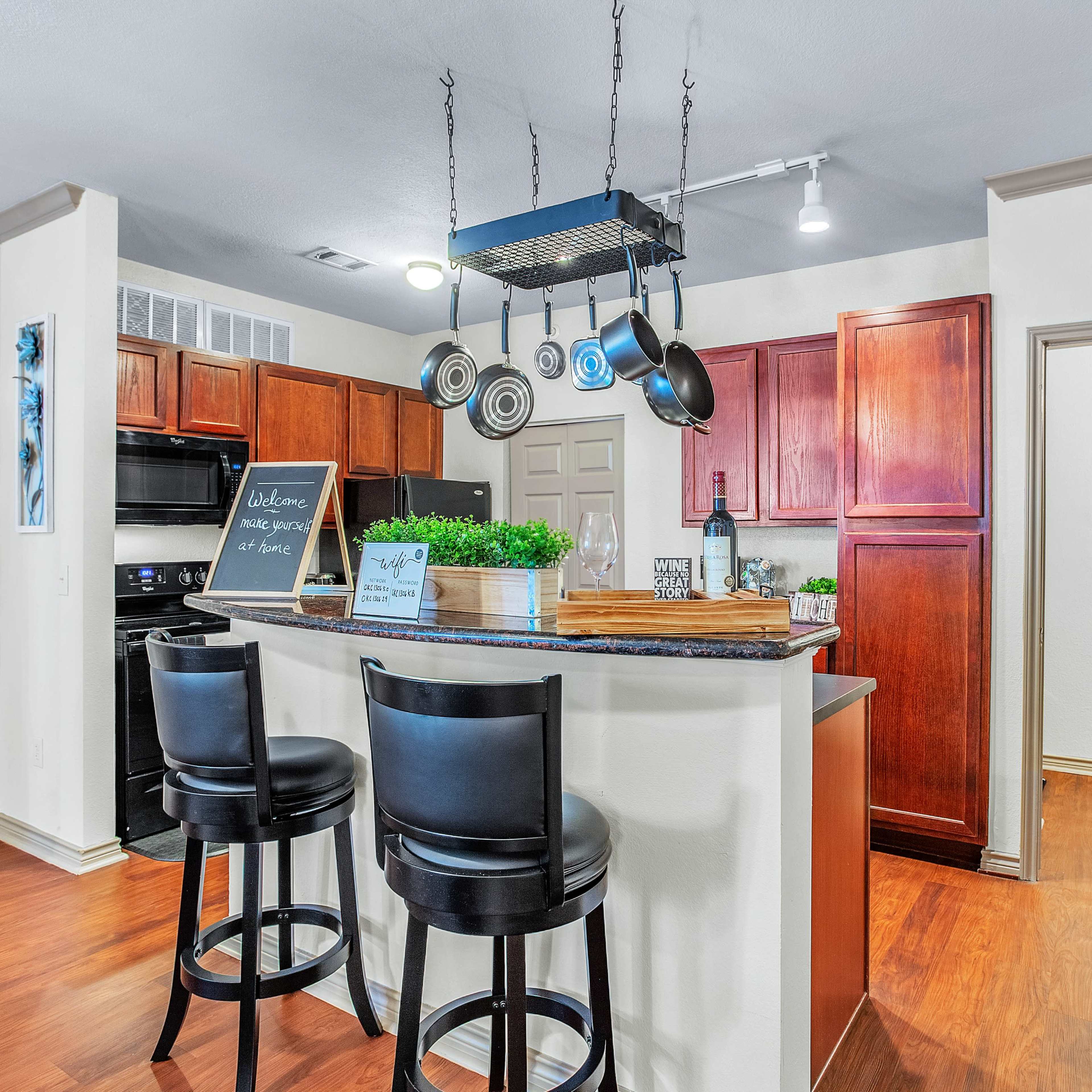 The kitchen features dark wood cabinets, a central island with bar stools, and hanging cookware above the counter.