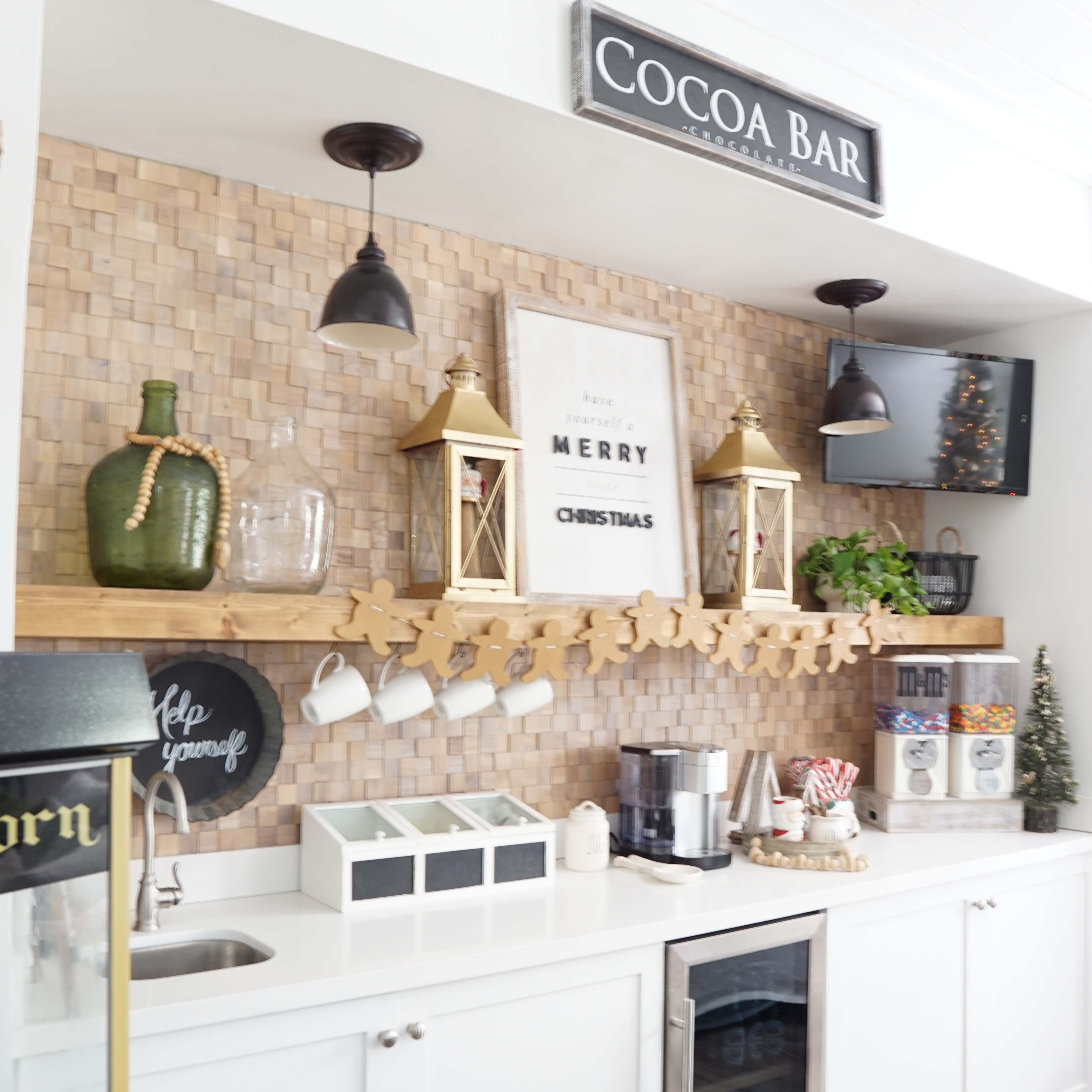 A kitchen area featuring a cocoa bar with decorative lanterns, a wooden shelf, and various containers arranged above a countertop.