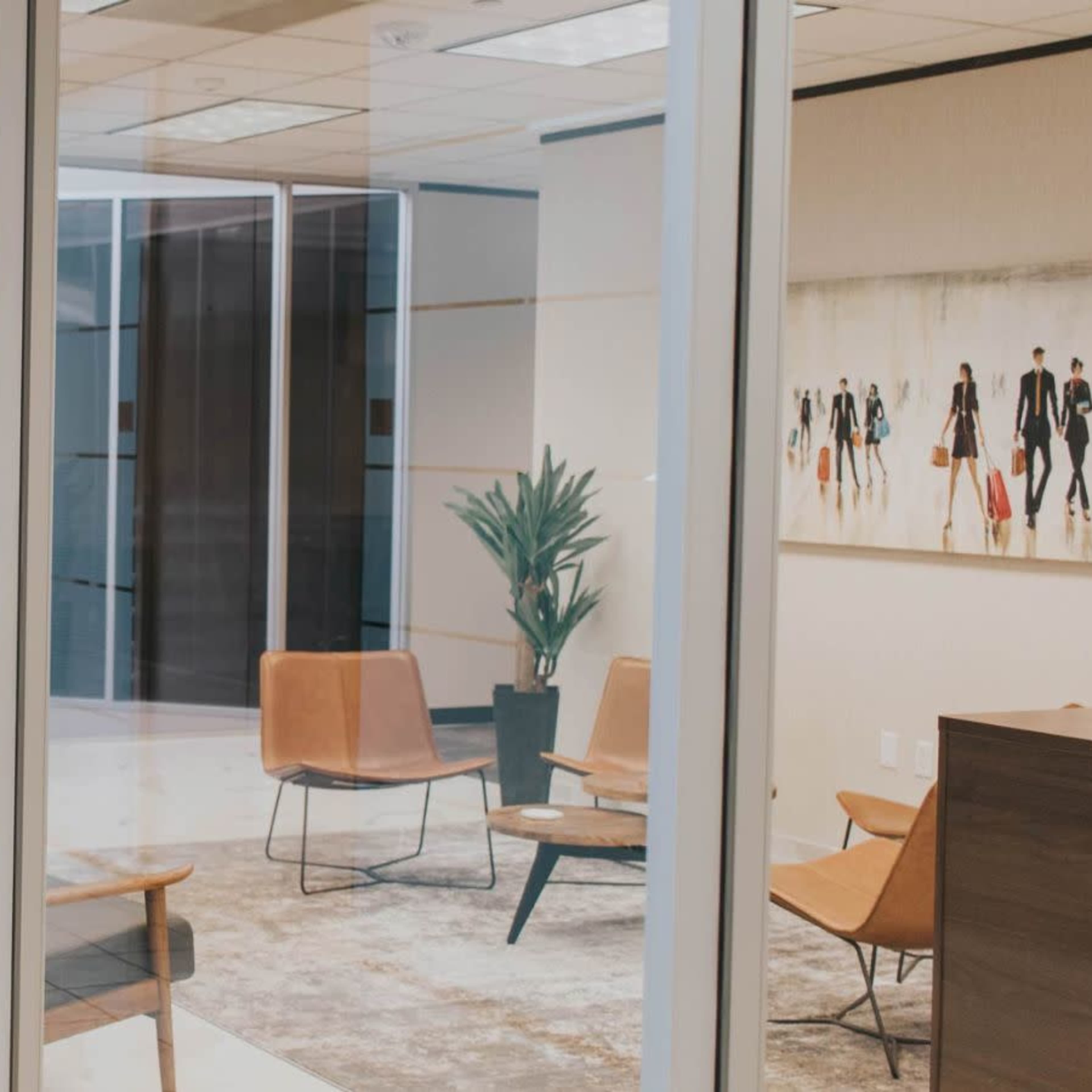 A modern office space with glass walls, featuring a seating area with four chairs and a decorative plant.