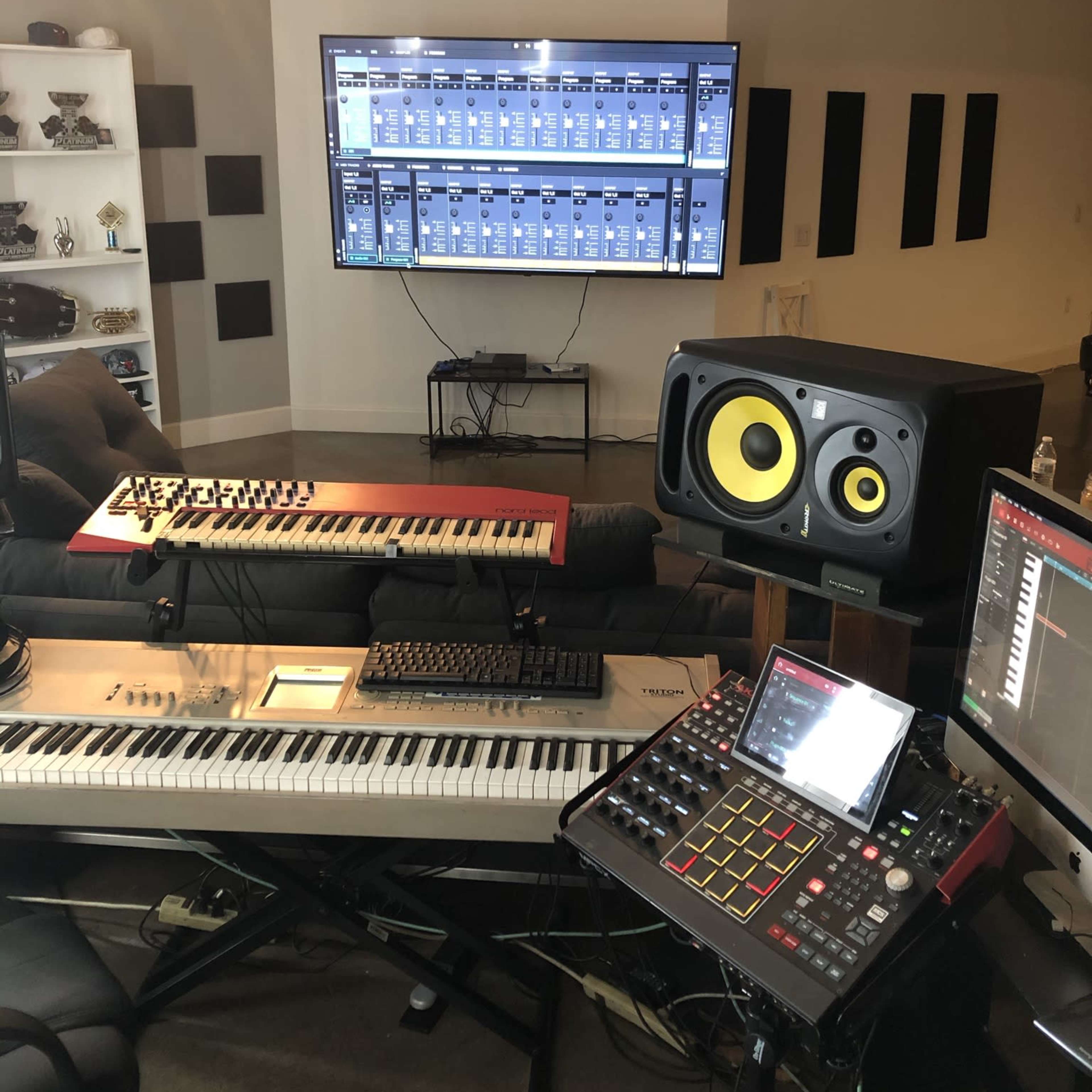 A music production studio featuring a keyboard, audio mixer, computer monitors, and various music equipment against a modern backdrop.