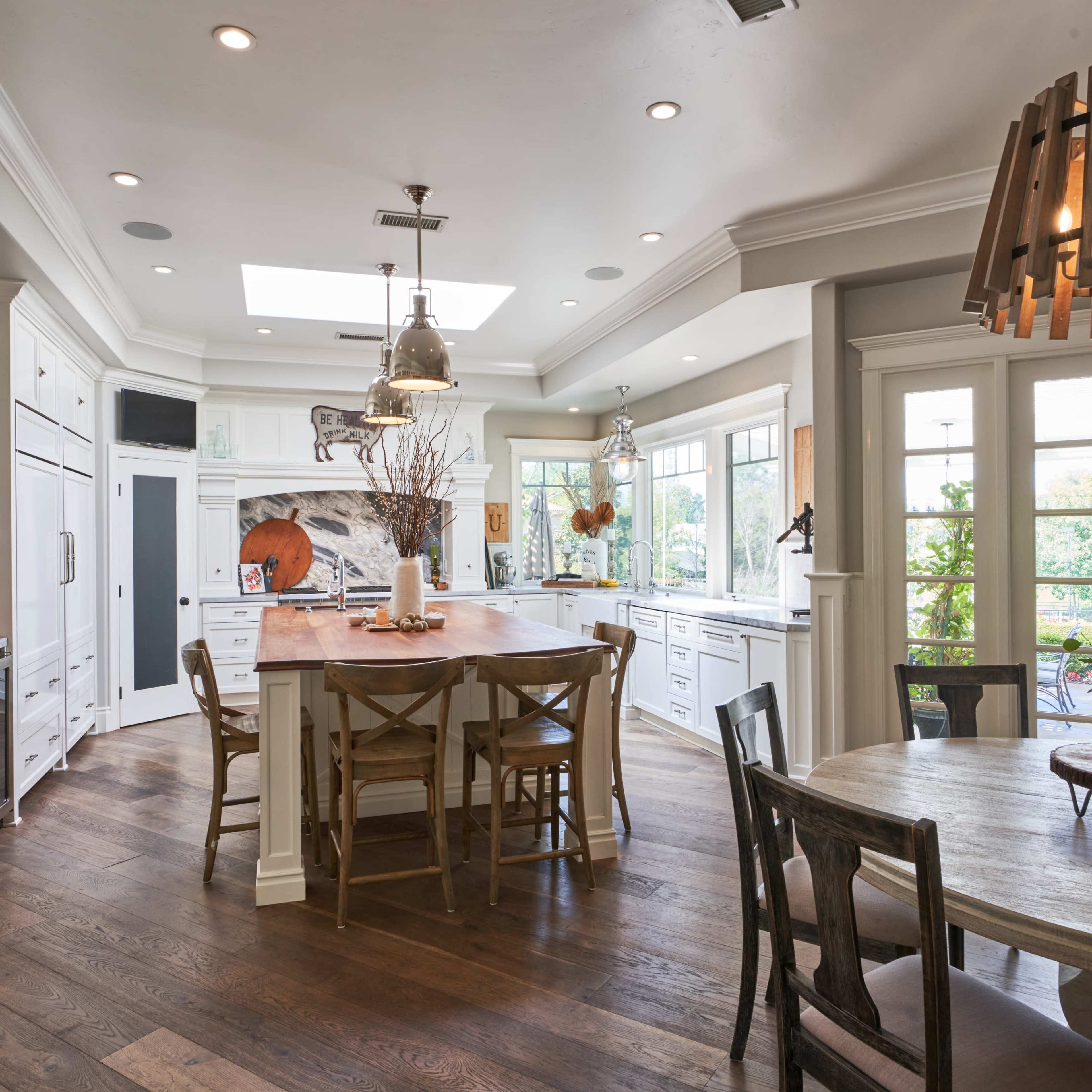 A spacious kitchen features white cabinetry, a large central island with seating, and a dining area with a round table and wooden chairs.
