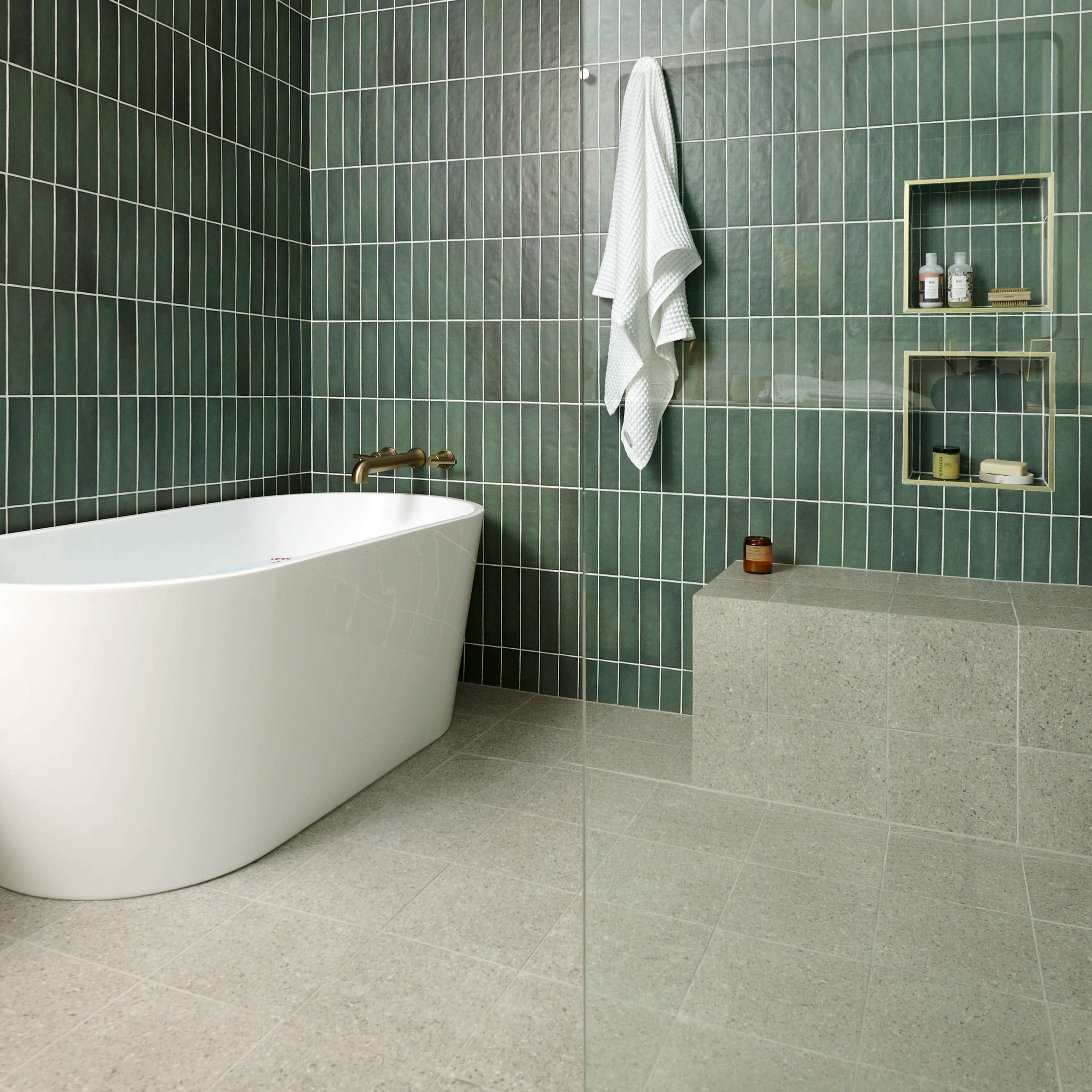 A modern bathroom featuring a freestanding white bathtub, green tiled walls, and a small wooden stool.