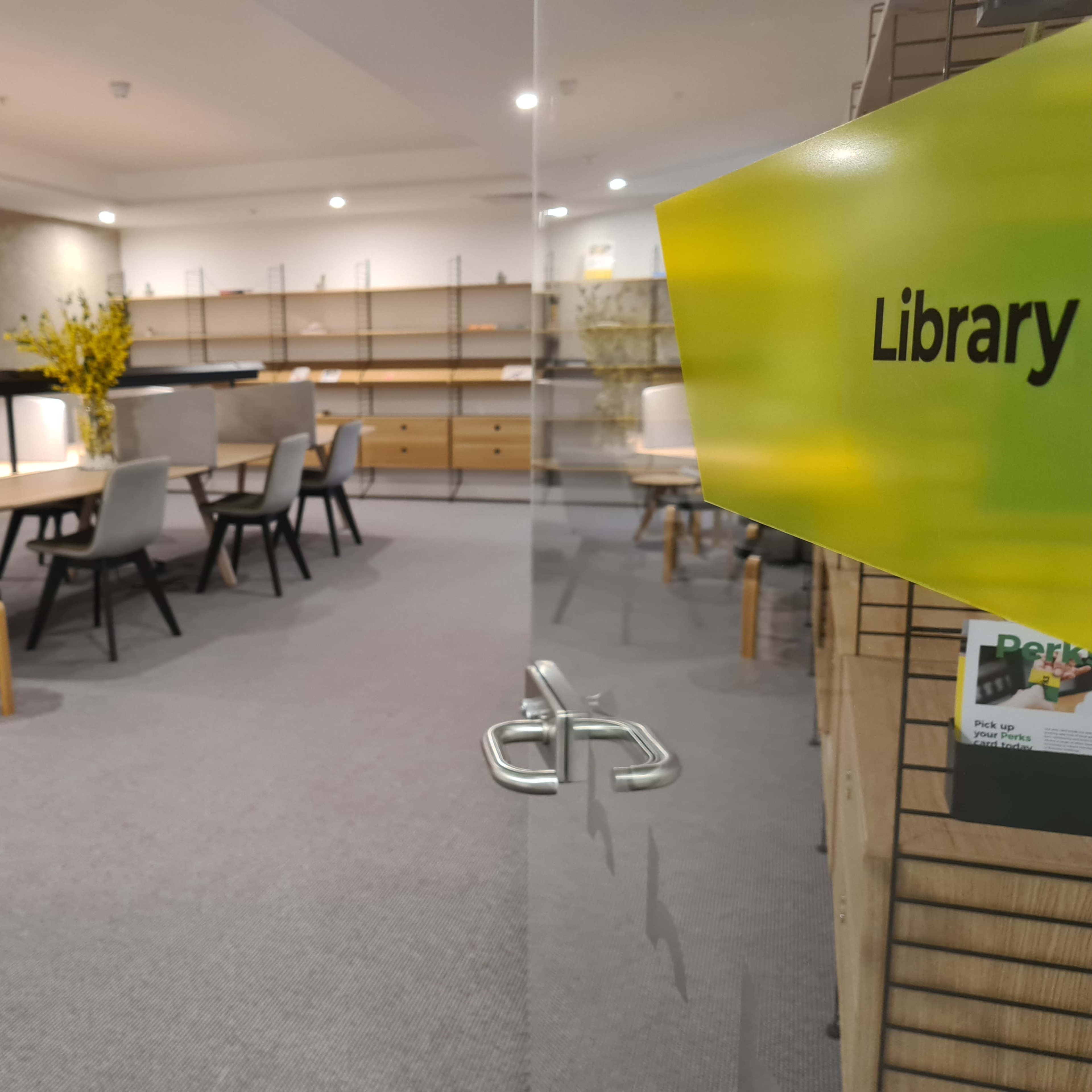 A modern library space featuring a large wooden table, several chairs, and shelves displaying books and decorative items.