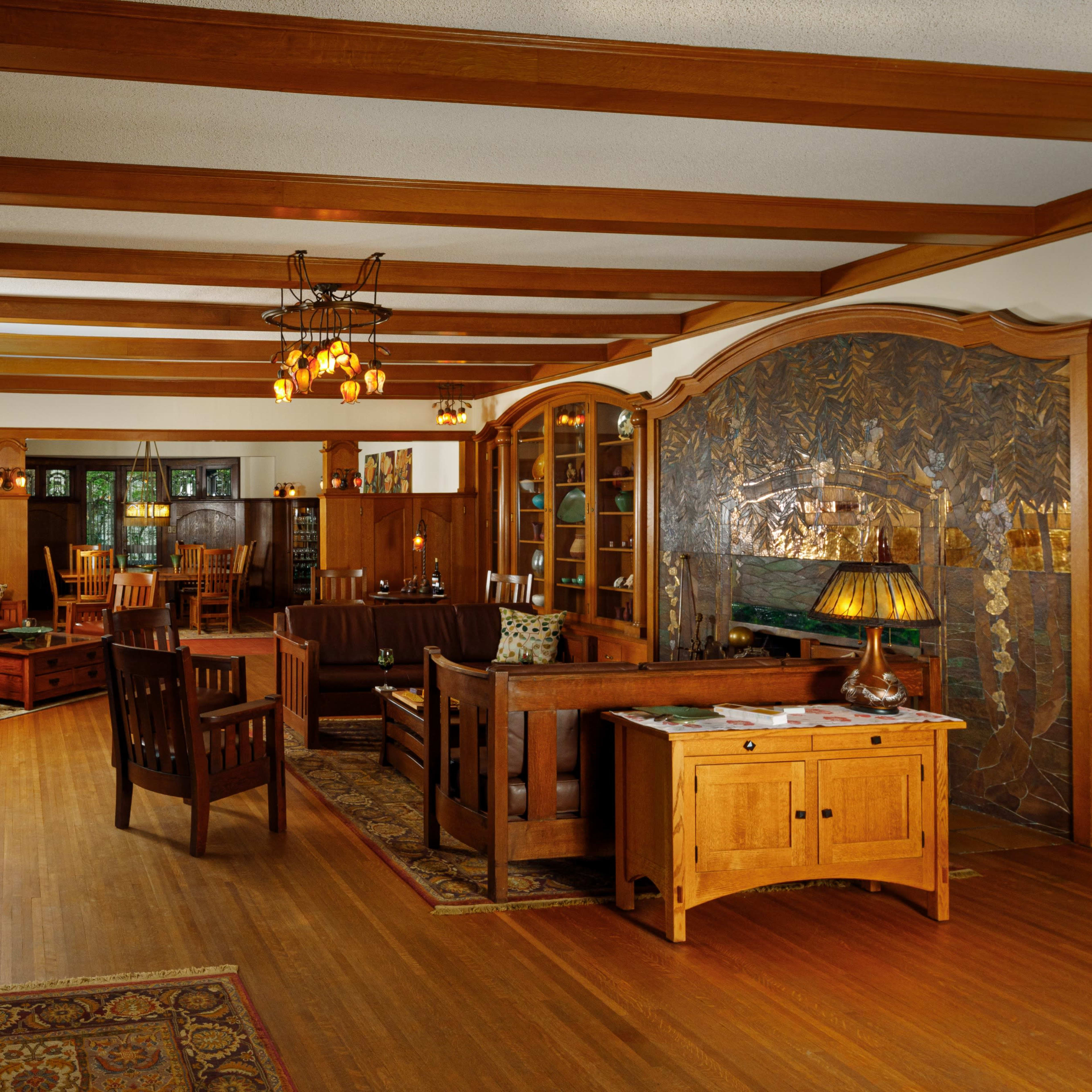 A warmly lit interior of a traditional living room featuring wooden furniture, a patterned rug, and decorative wall art.
