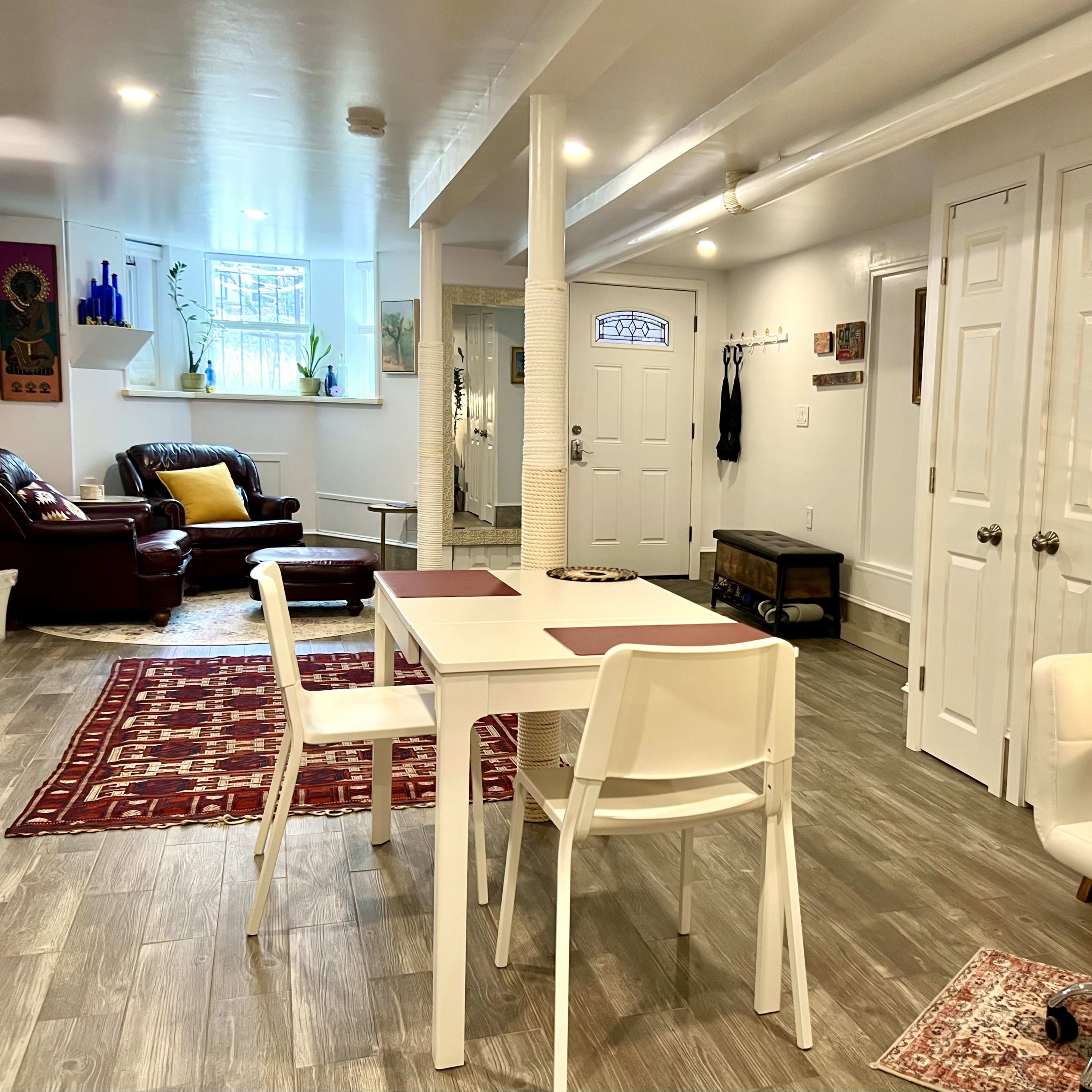 A well-lit room featuring a dining table with chairs, a seating area with a couch, and various decorative elements on the walls.