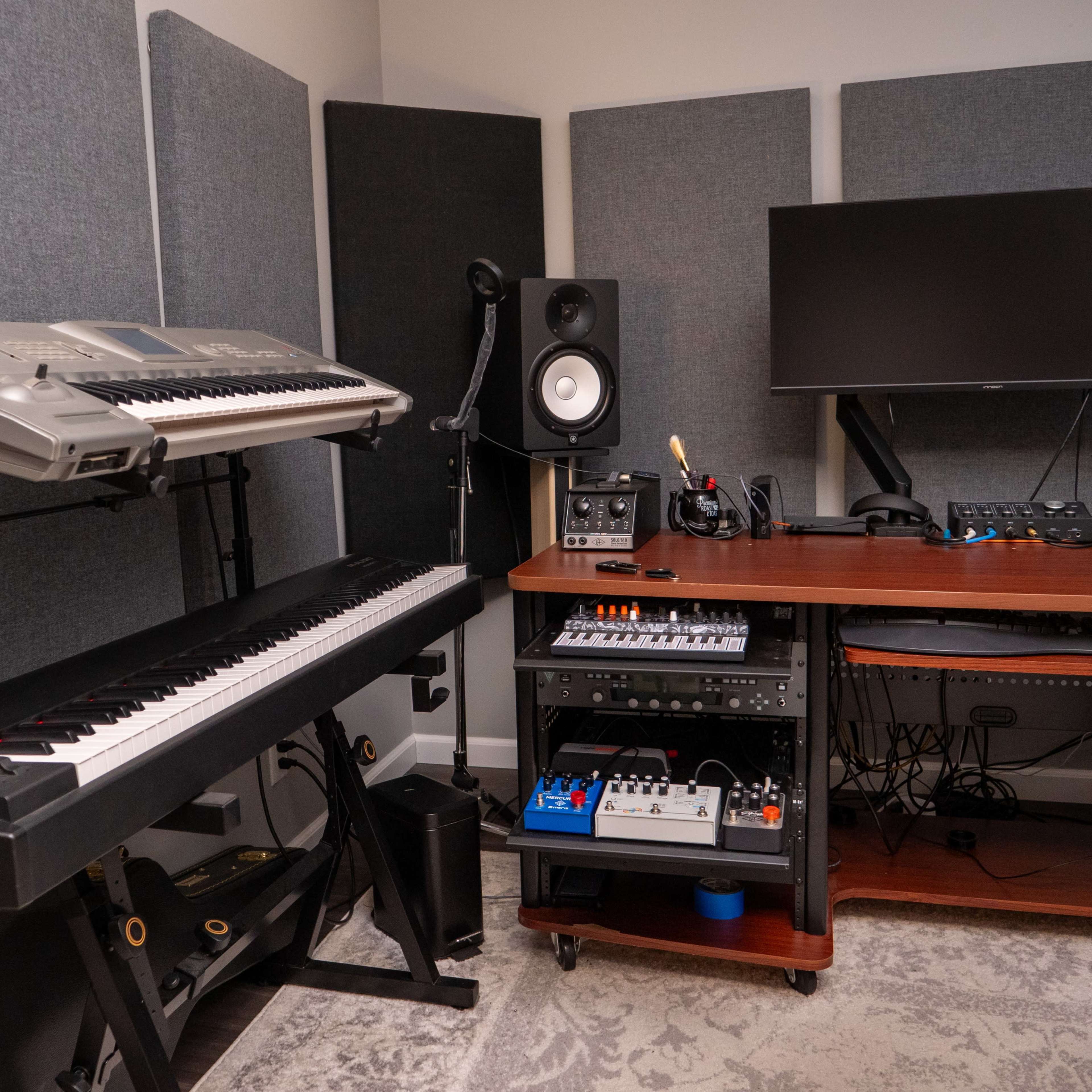 A music production setup featuring a keyboard, audio interface, monitor speakers, and a computer desk with various equipment in a sound-treated room.