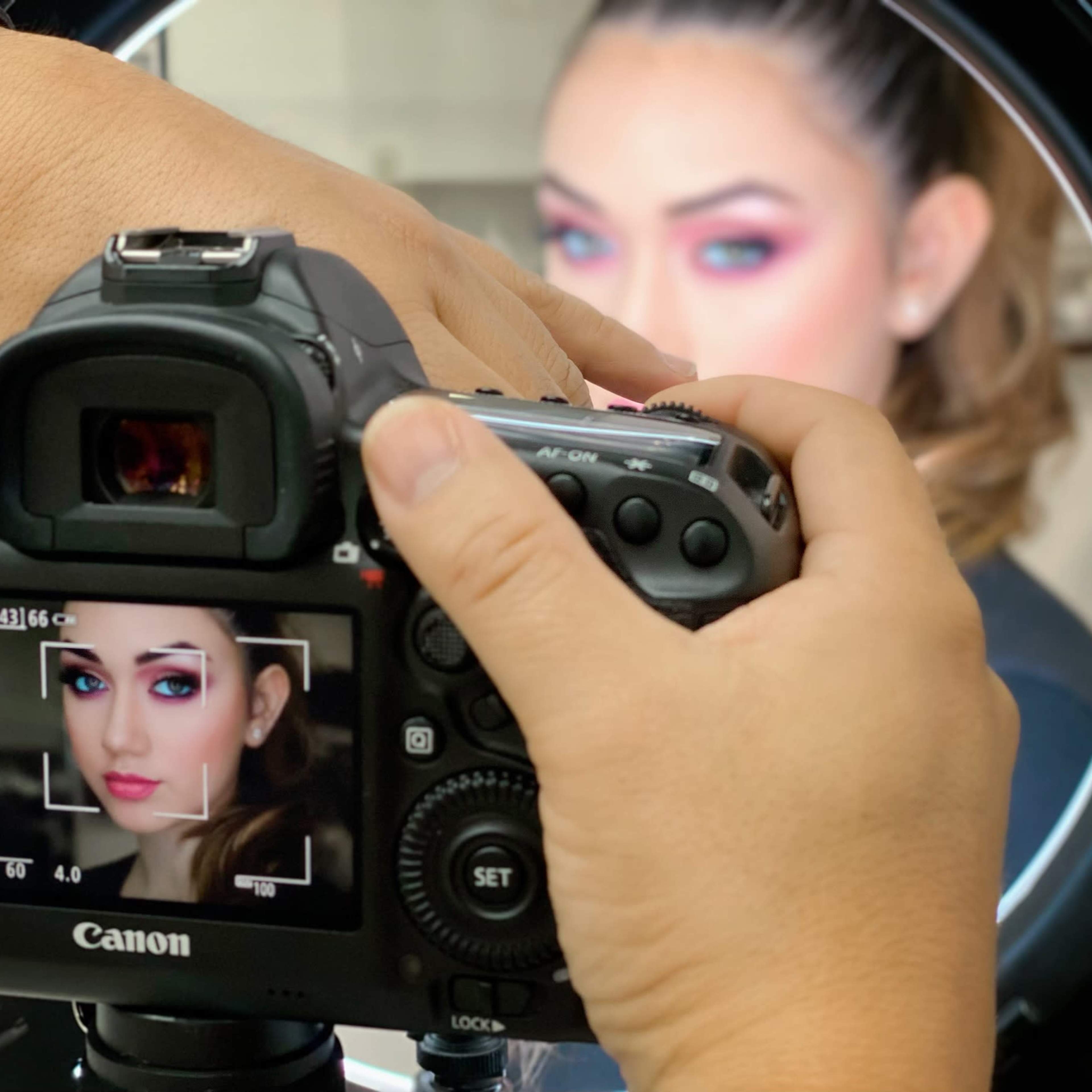 A person is using a Canon camera to photograph a model being illuminated by a ring light.