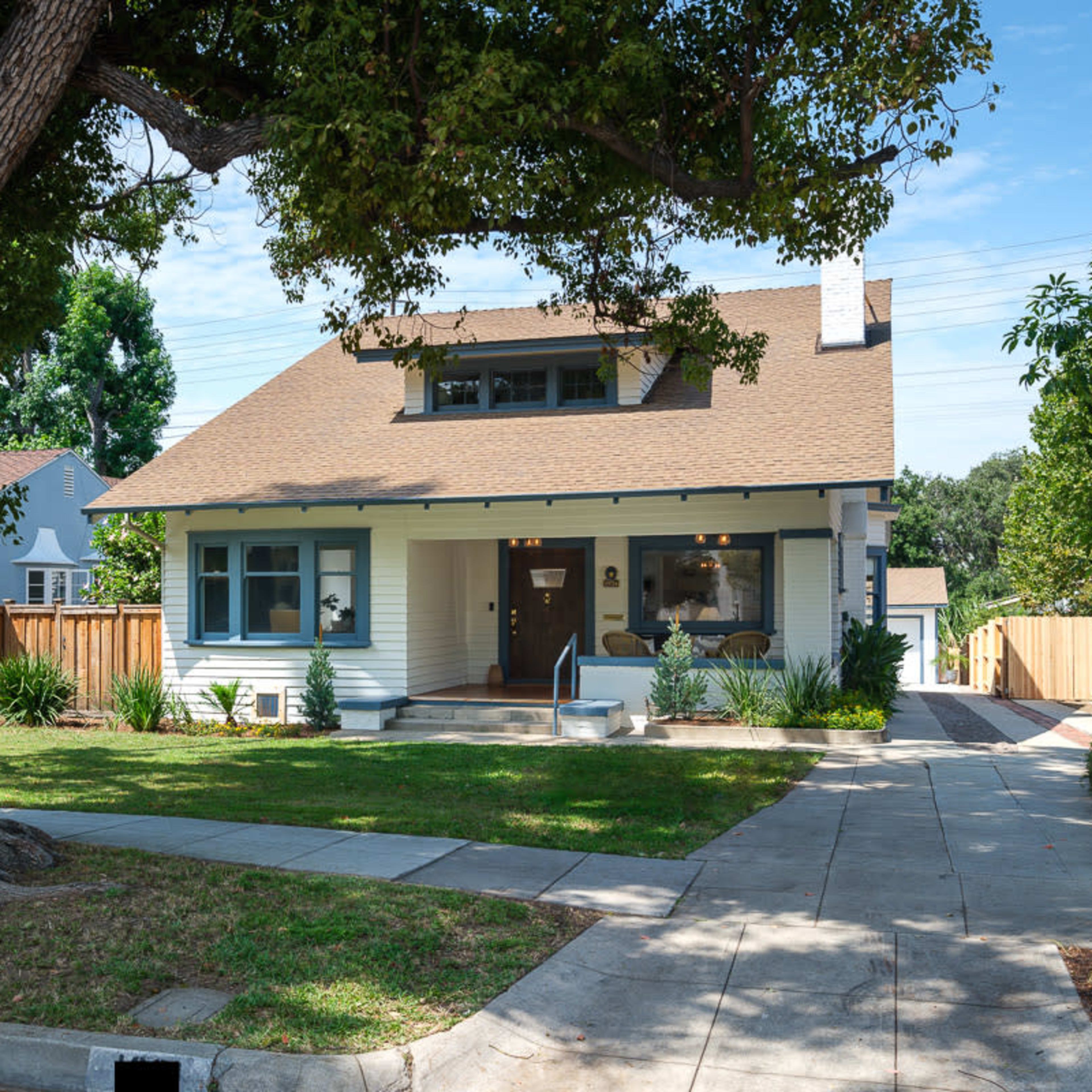 A two-story house with a pitched roof and blue siding is set in a landscaped yard with trees and shrubs.