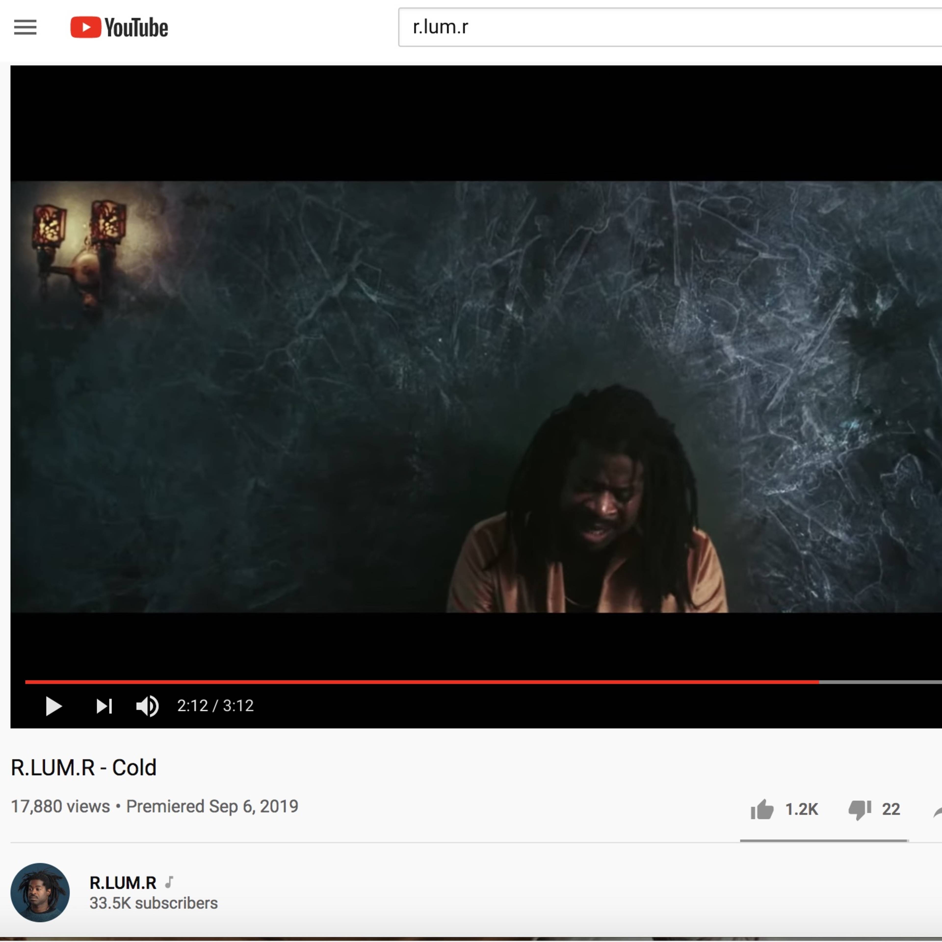 A YouTube video titled "R.I.U.M.R - Cold," featuring a man with long hair sitting against a textured blue background, under wall-mounted lights.