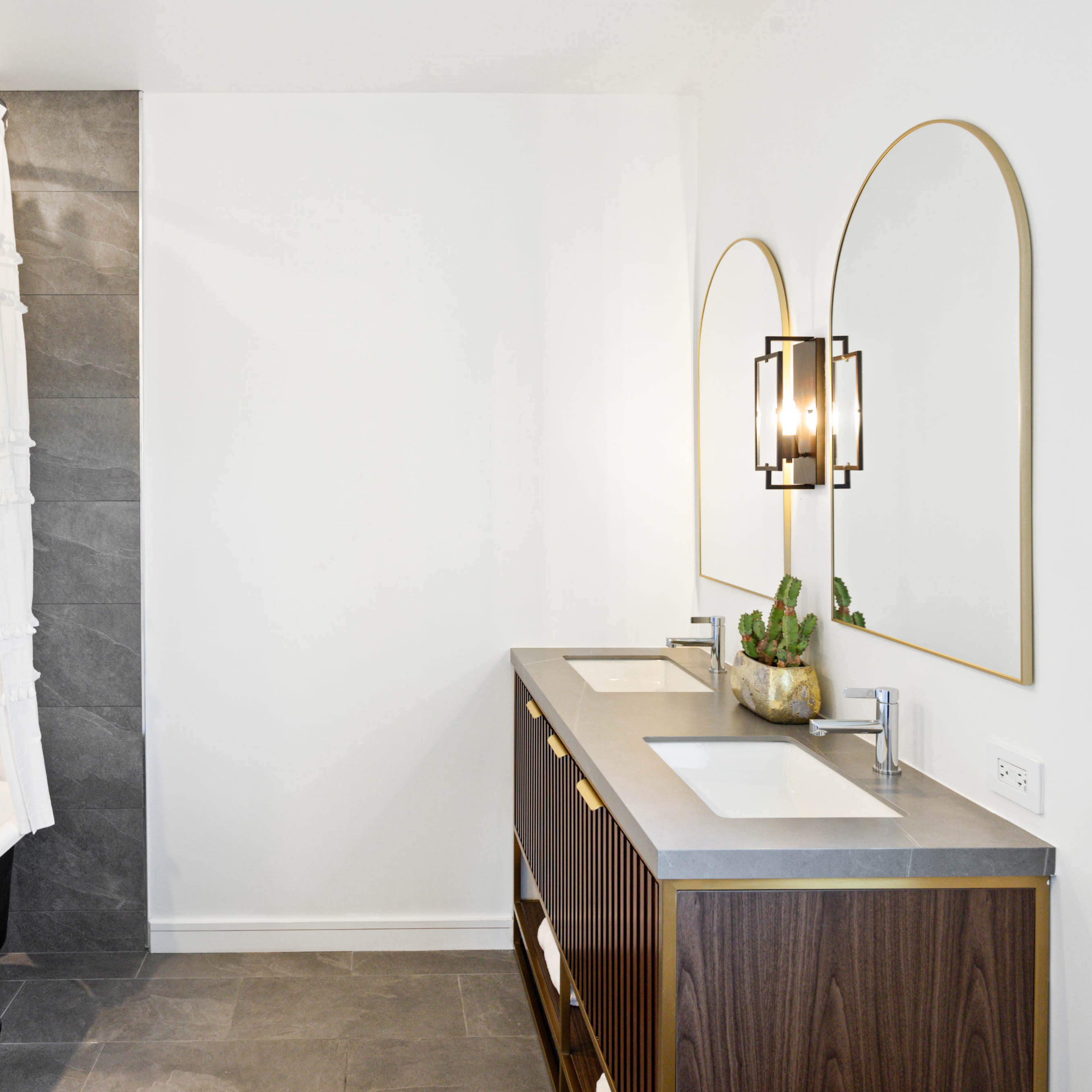 A modern bathroom features a freestanding bathtub, a double-sink vanity with a gray countertop, and two illuminated mirrors above it.