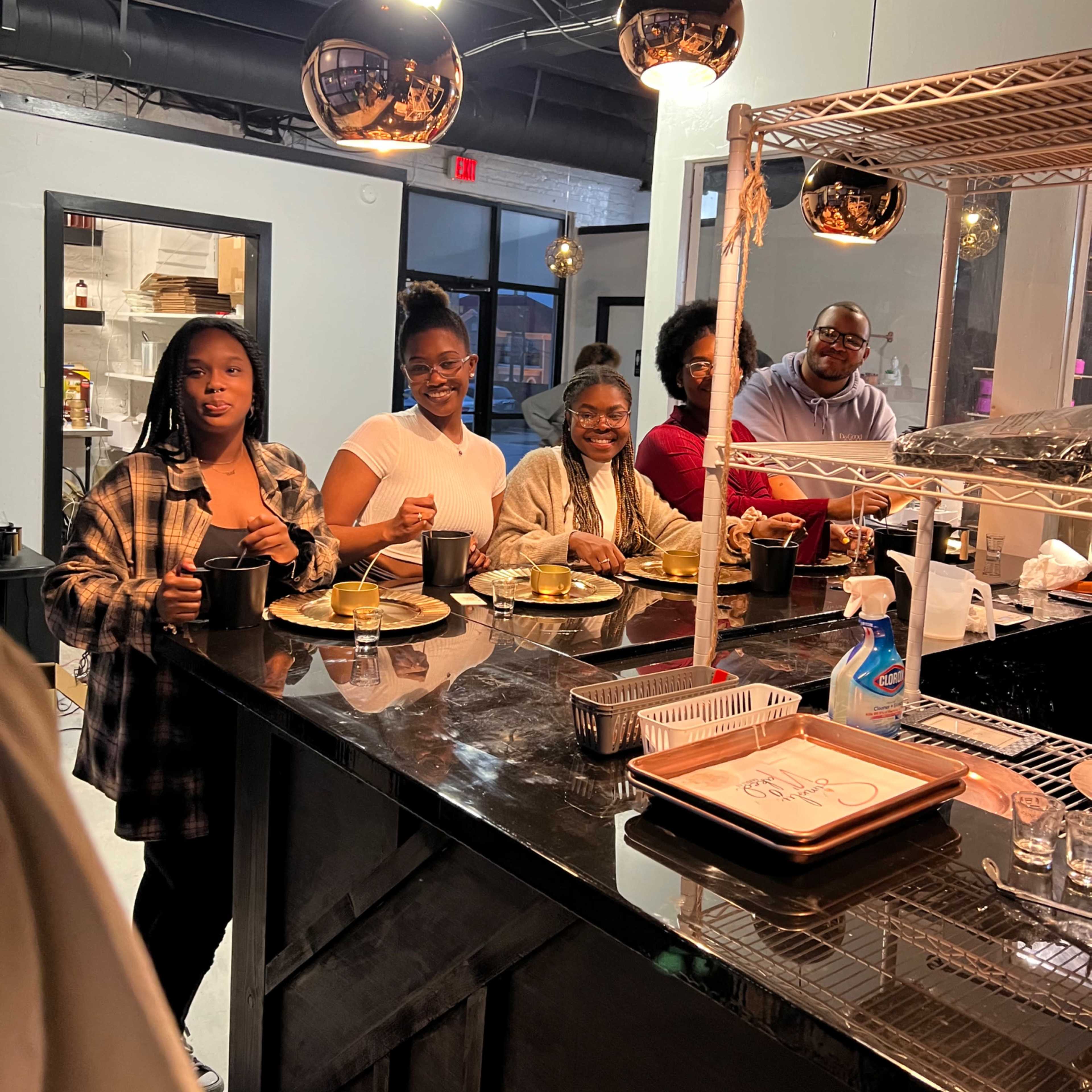 A group of five people sits at a bar counter in a modern restaurant, enjoying their meals and drinks.
