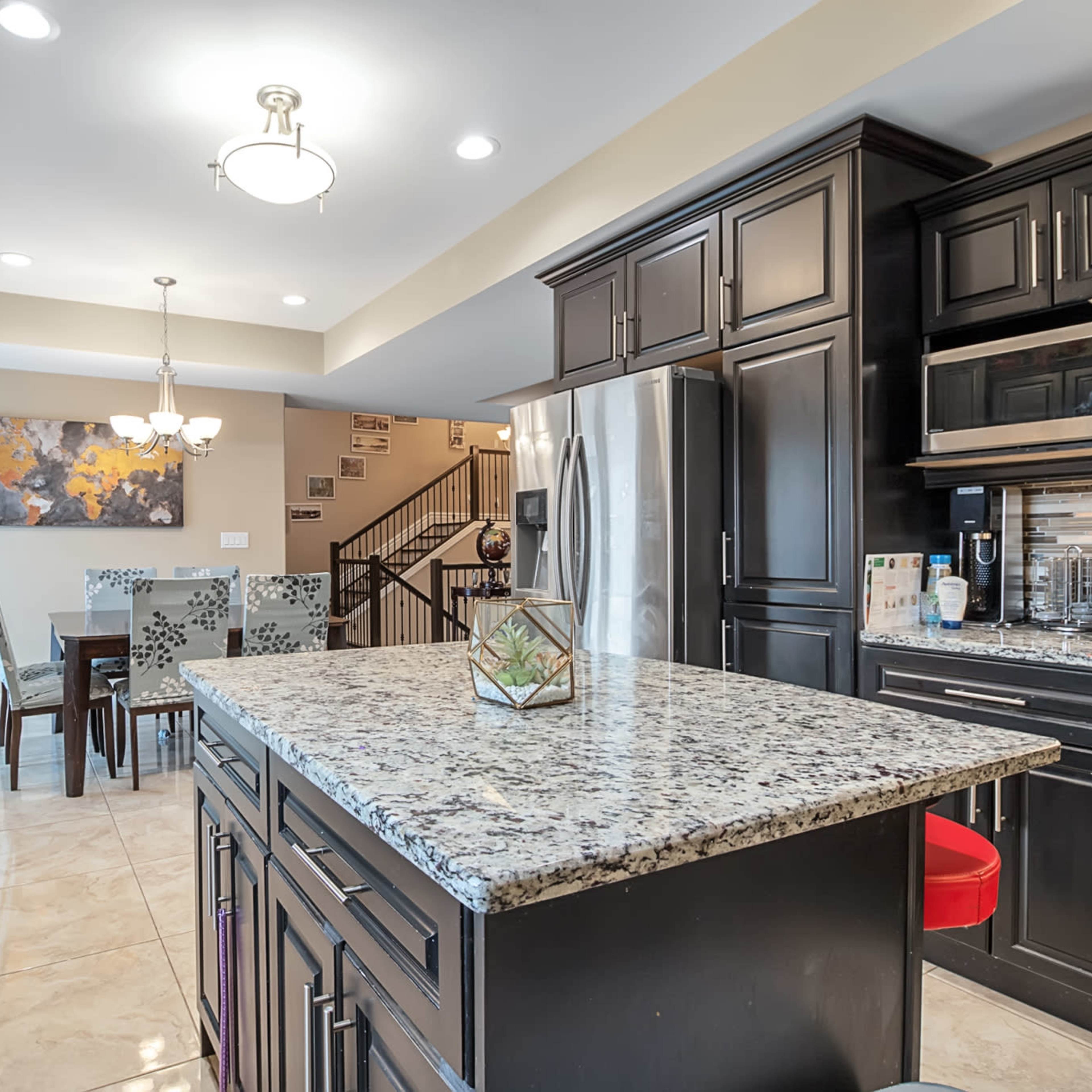 A modern kitchen with dark cabinetry and a granite countertop, adjacent to a dining area with a table and chairs.