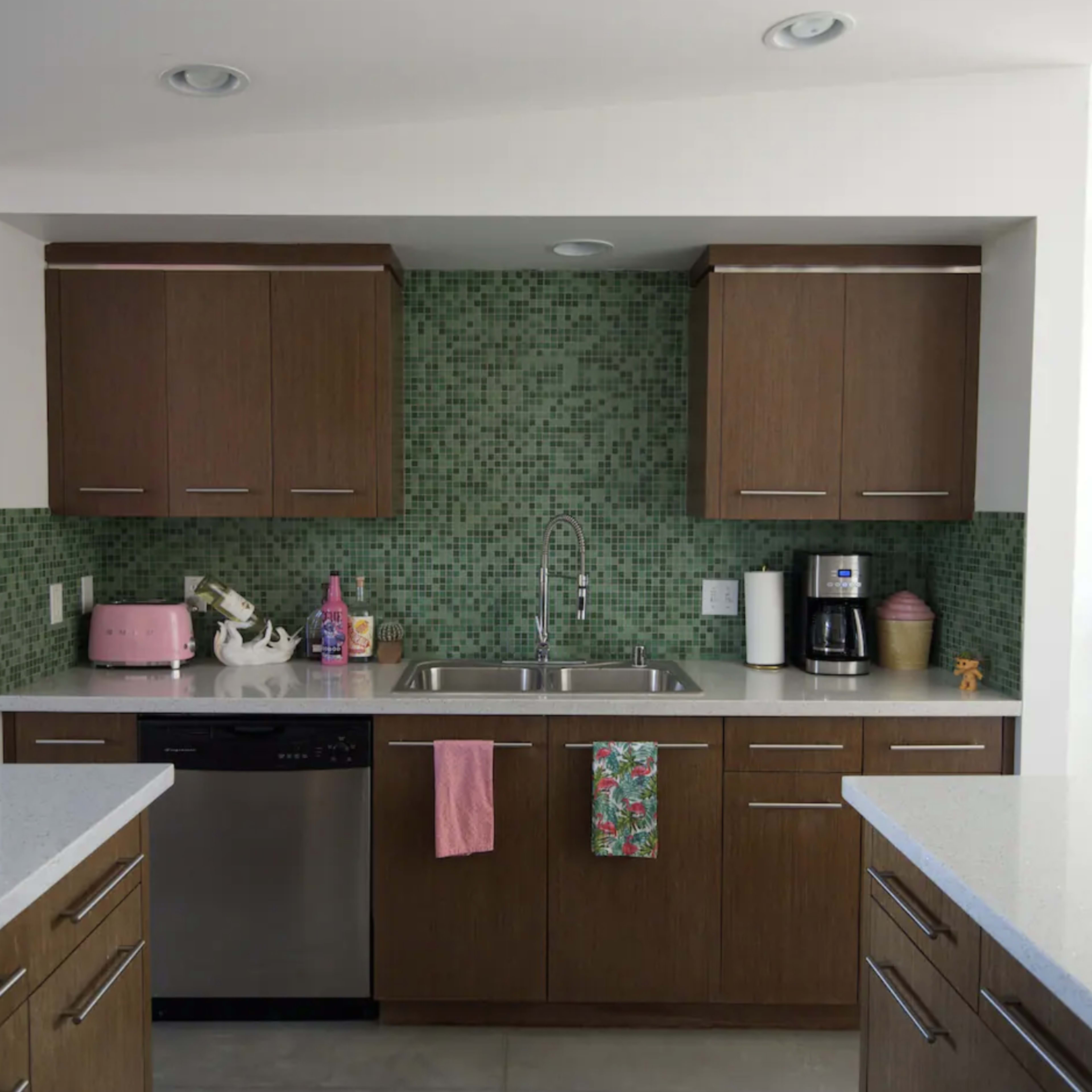 A modern kitchen featuring wooden cabinets, a mosaic green backsplash, and stainless steel appliances, including a dishwasher and coffee maker.