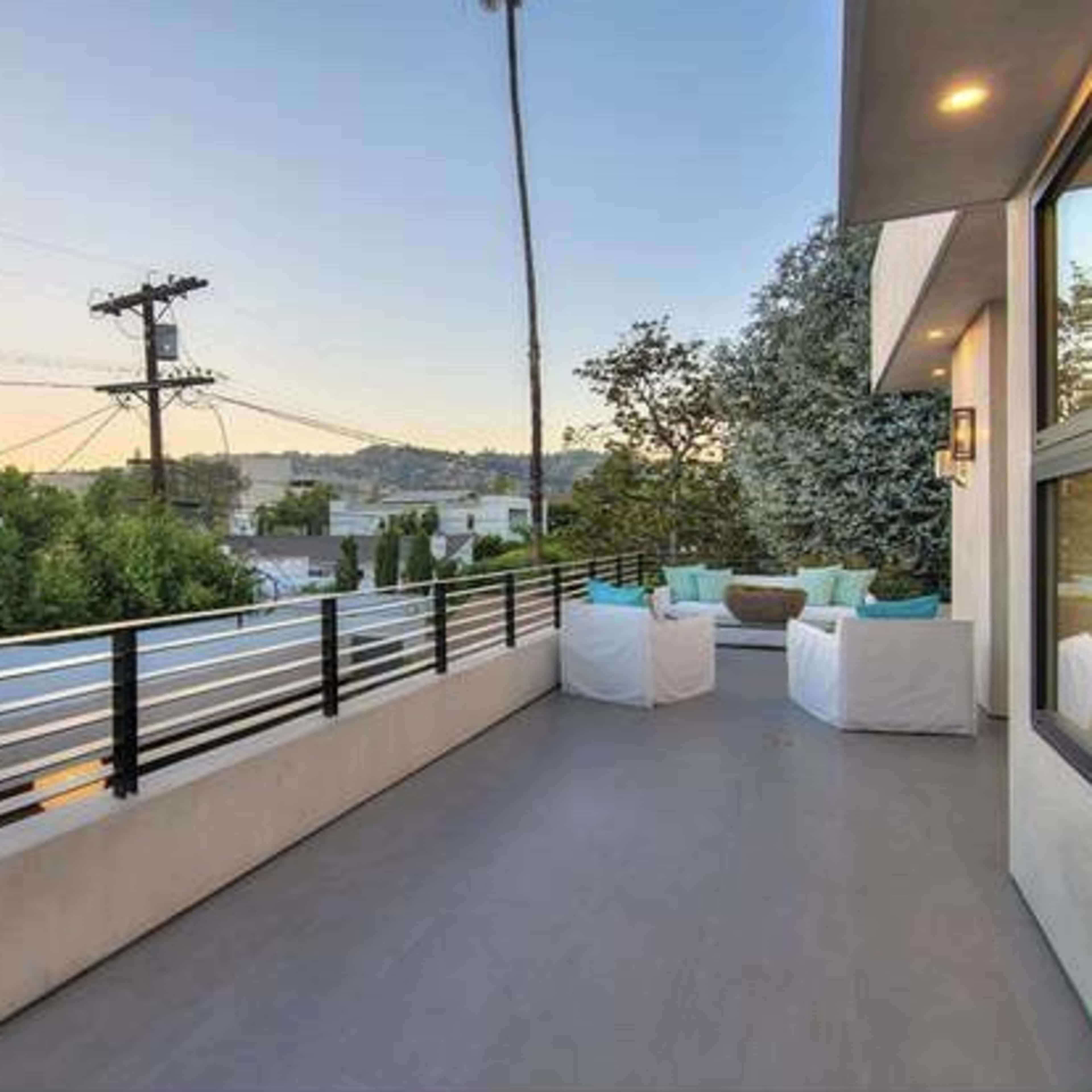 A modern balcony with minimalist seating, overlooking trees and utility poles against a clear sky.
