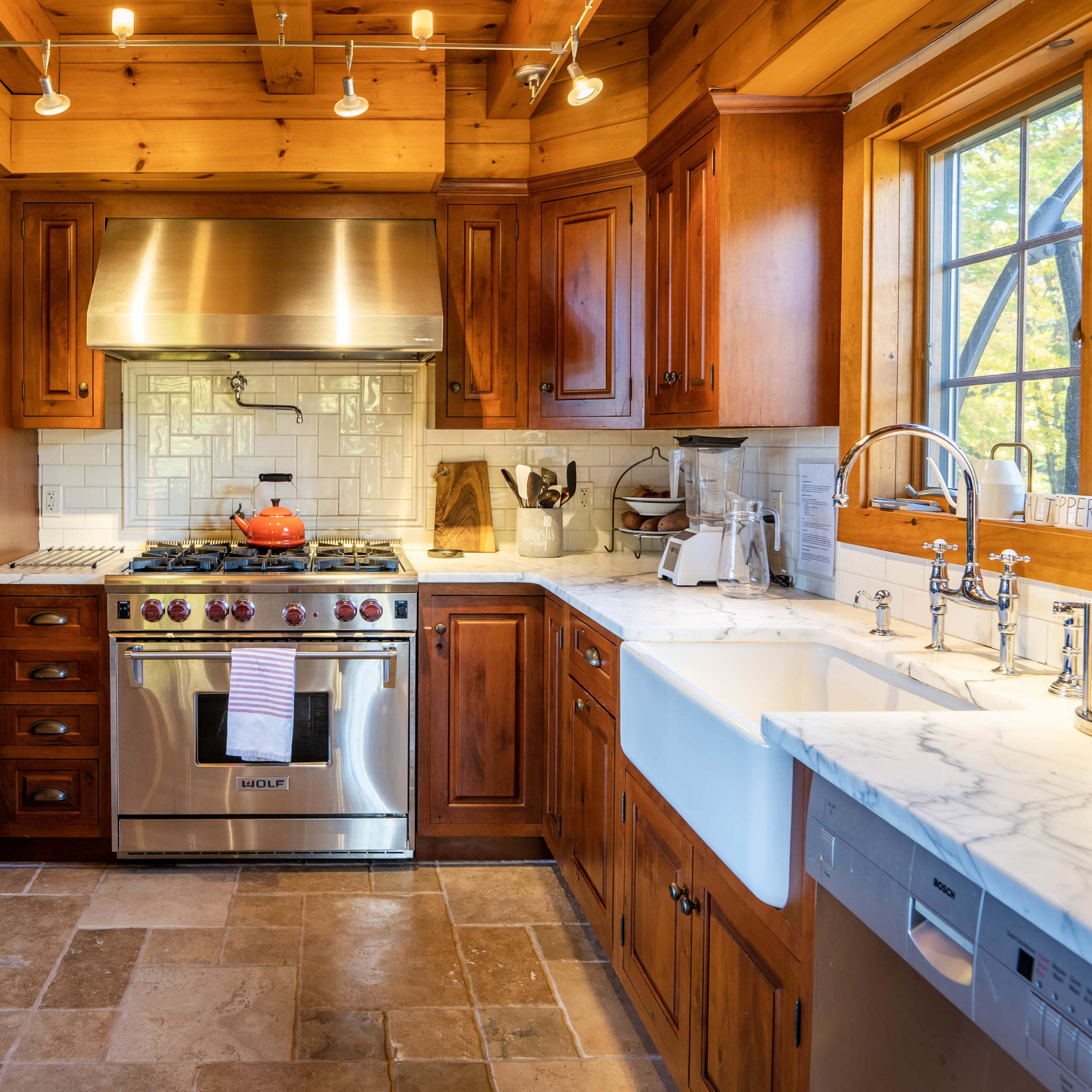 A modern kitchen features wooden cabinetry, stainless steel appliances, and a large farmhouse sink with marble countertops.