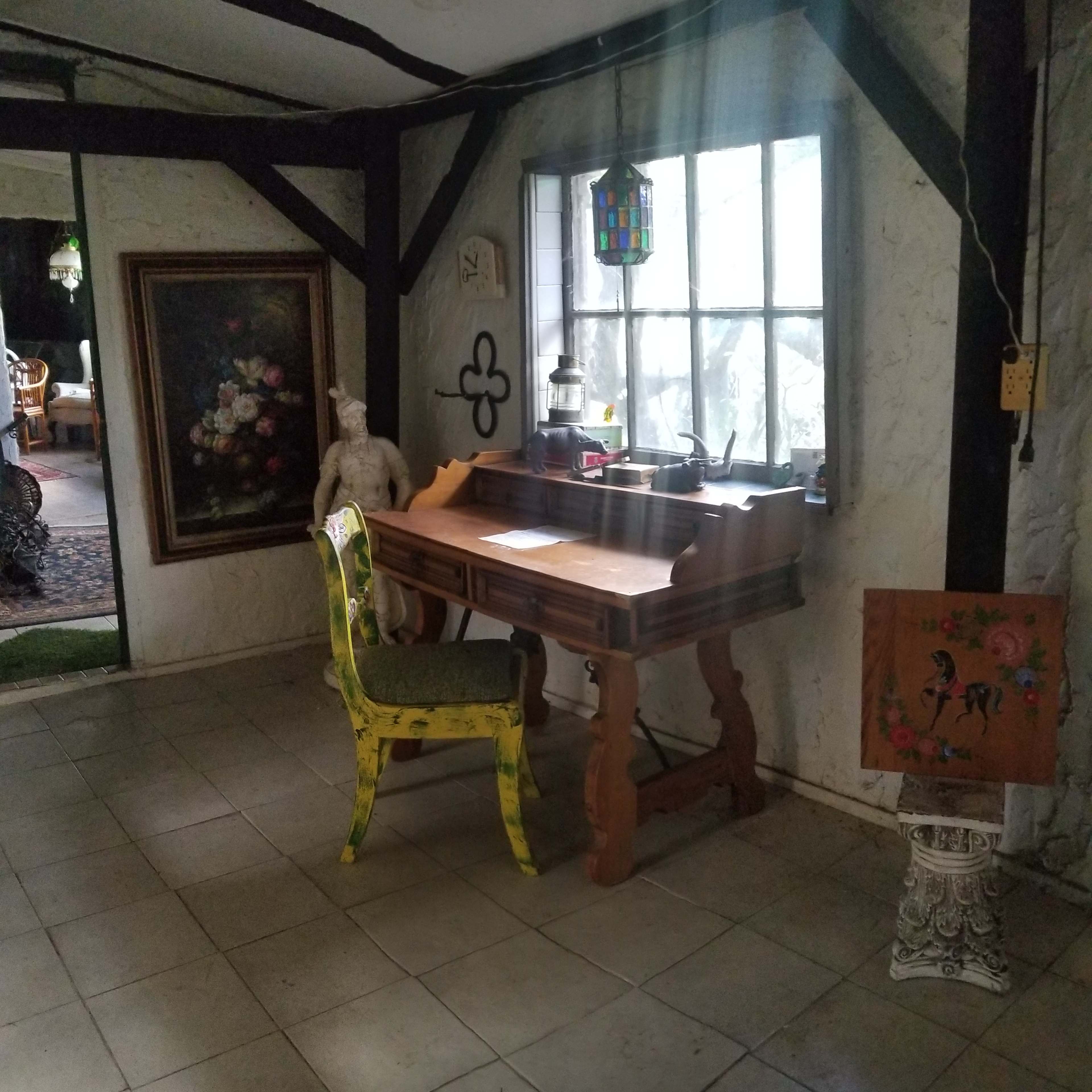A wooden desk with a yellow chair beside a window in a room featuring rustic decor and artwork on the walls.