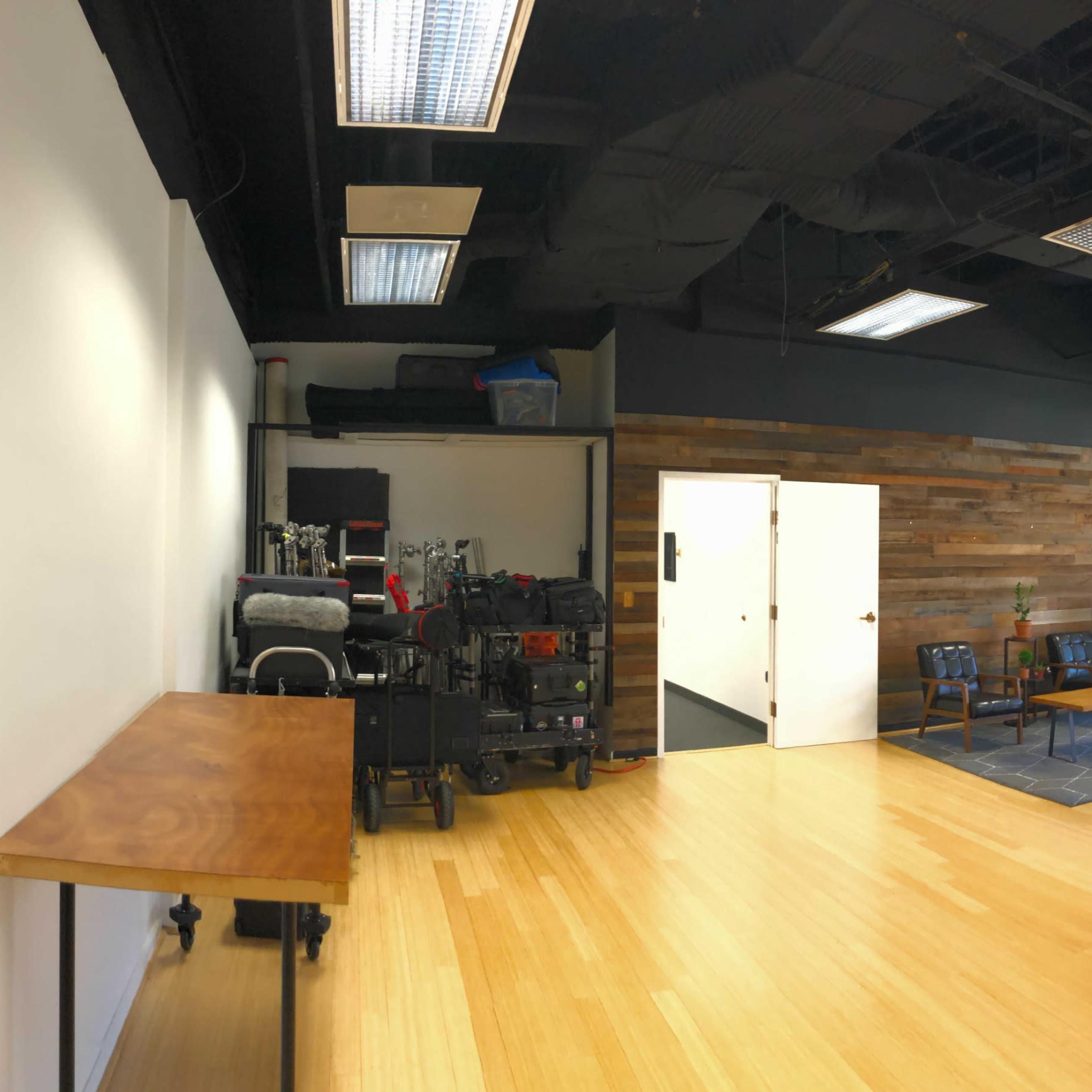 A spacious interior of an office or studio with wooden flooring, a wall of wooden panels, and various equipment stored on one side.