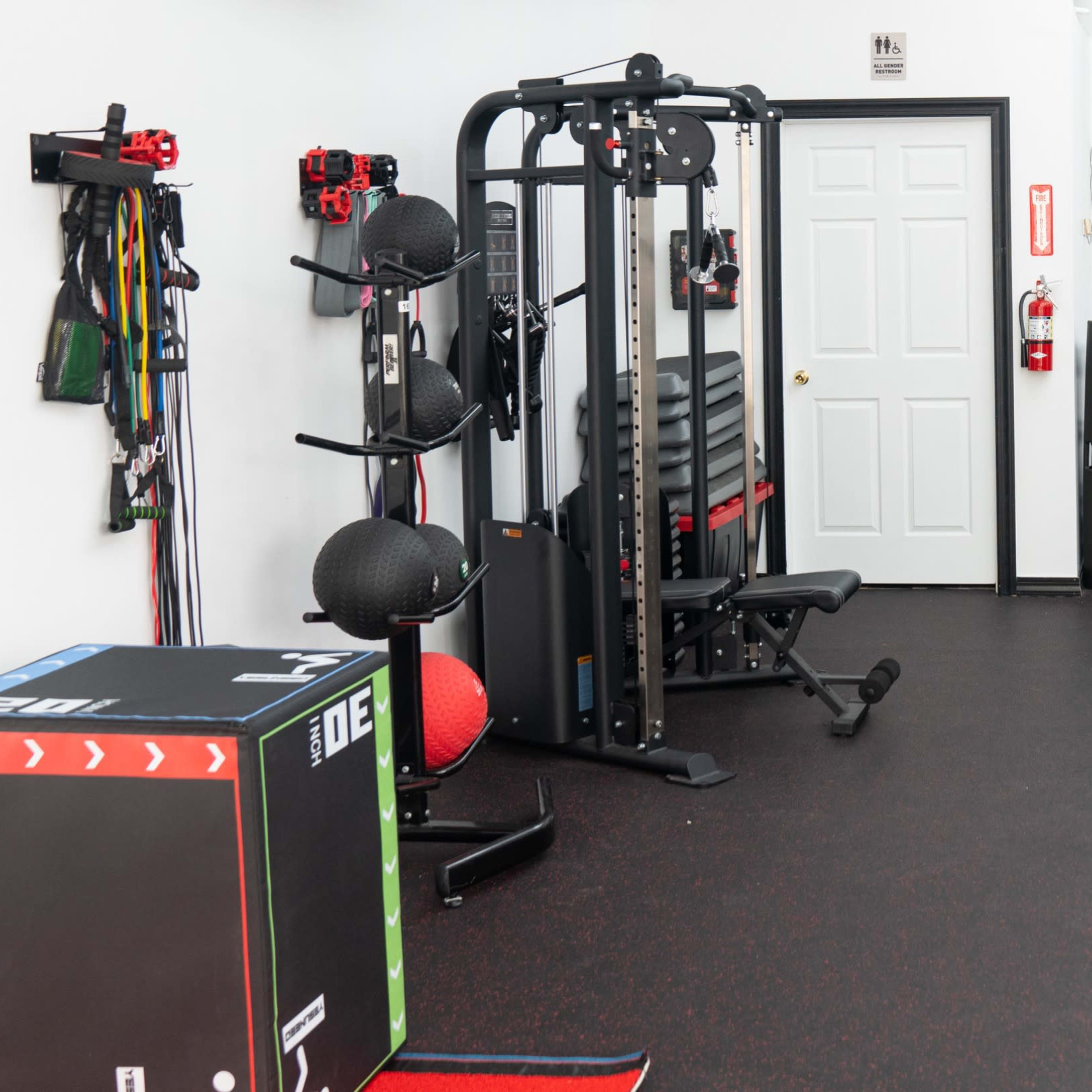 A gym interior featuring various exercise equipment, including weight racks, benches, and a boxing-themed mural on the wall.