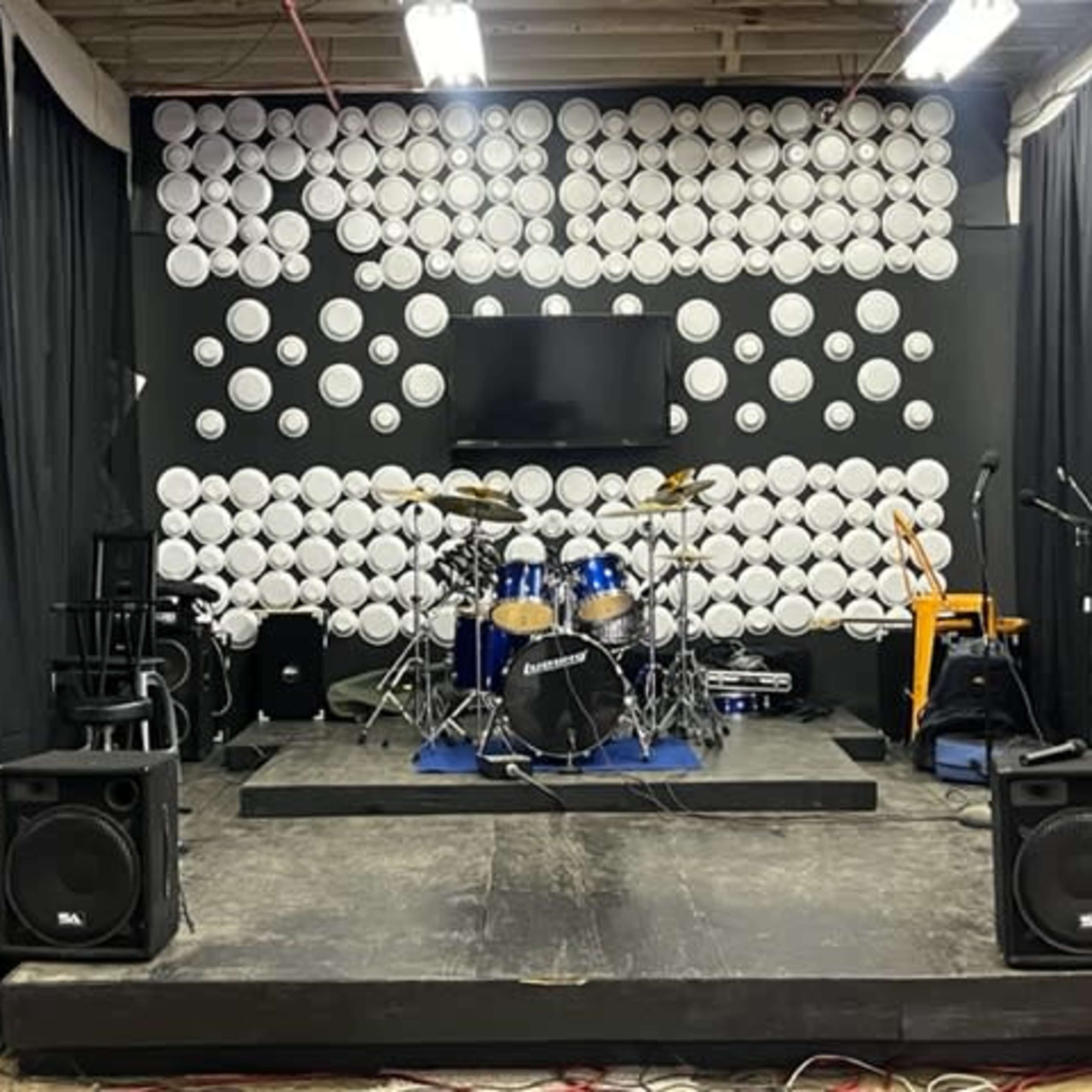 A stage setup with a drum kit, amplifiers, and instruments against a backdrop of white circular decorations.